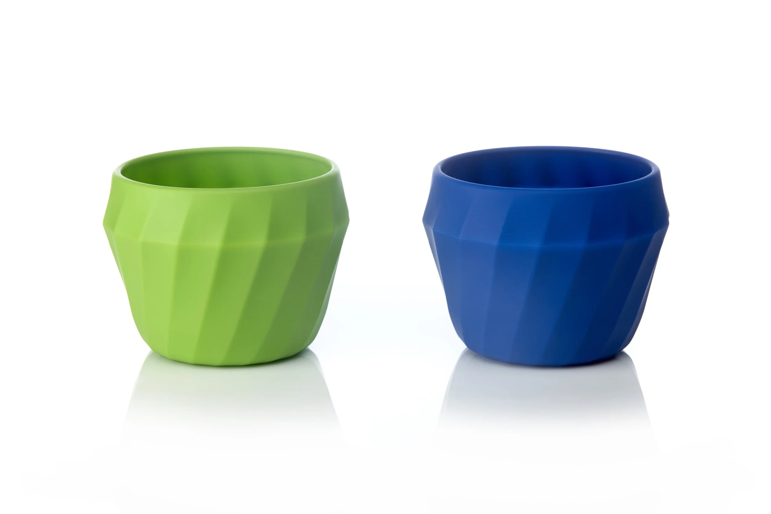 Two colorful cups, one green and one blue, with a faceted design, placed side by side on a reflective white surface.