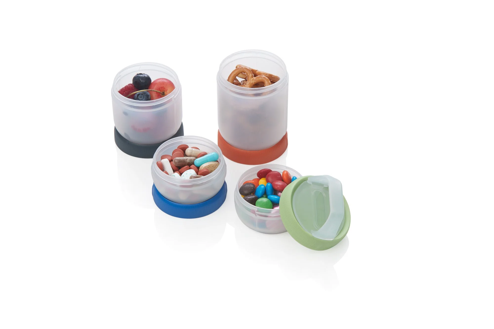 Four plastic containers with colored lids, filled with various snacks including berries, pretzels, pills, and candy.