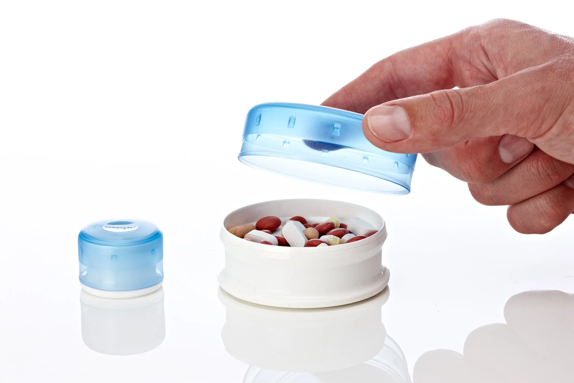 Hand opening a blue pill container filled with various tablets and capsules.