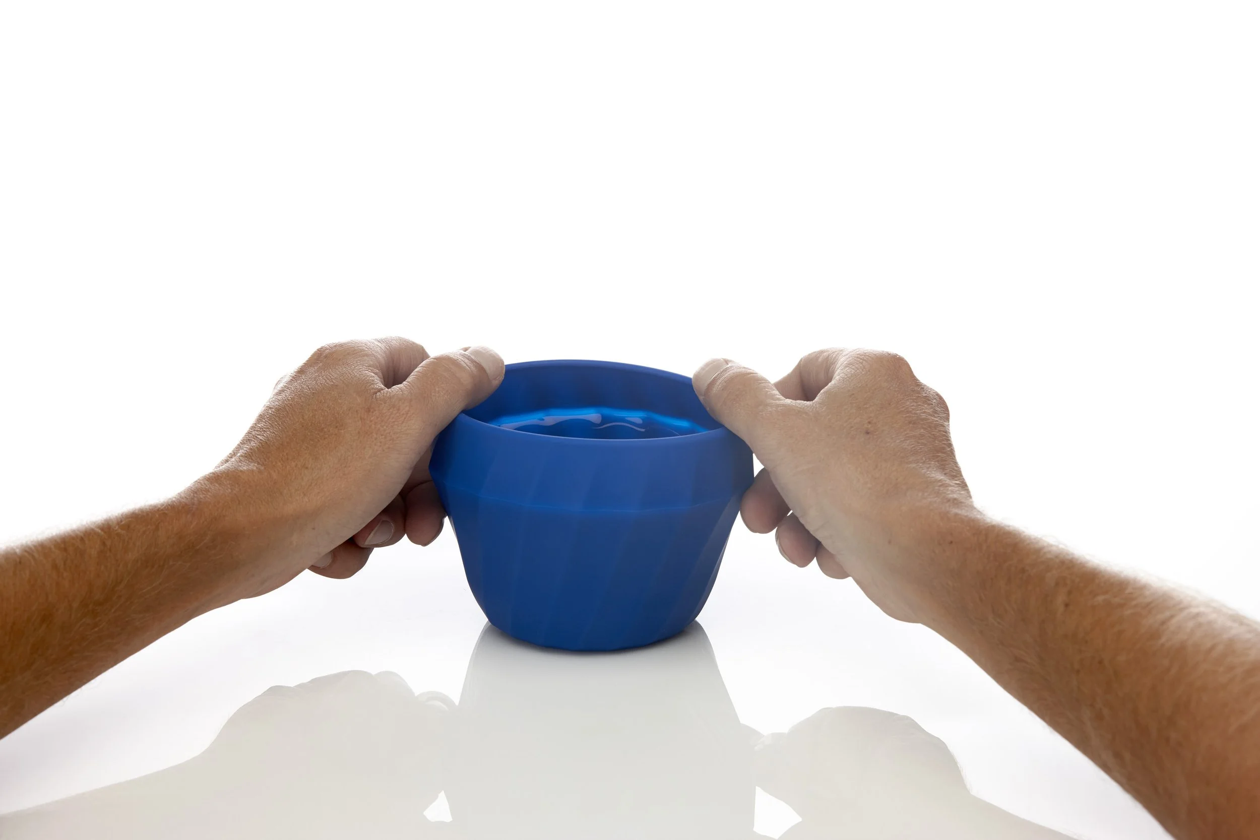 Hands holding a blue silicone mold on a reflective surface.