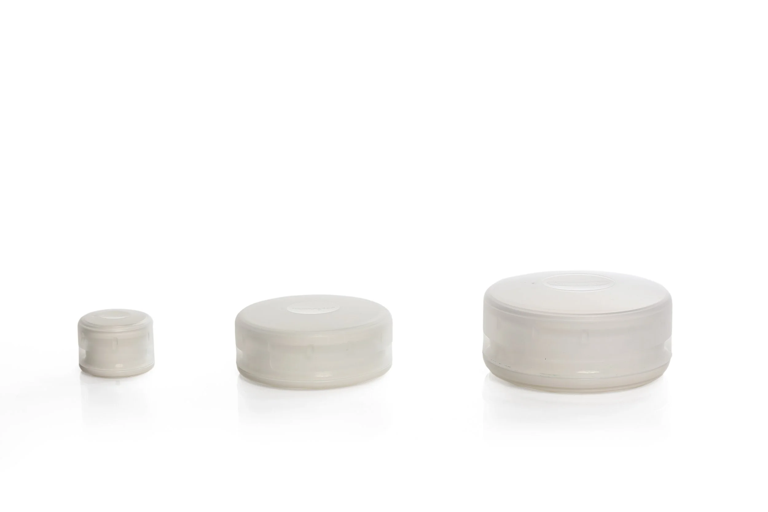Three different sizes of white plastic caps lined up on a white background.