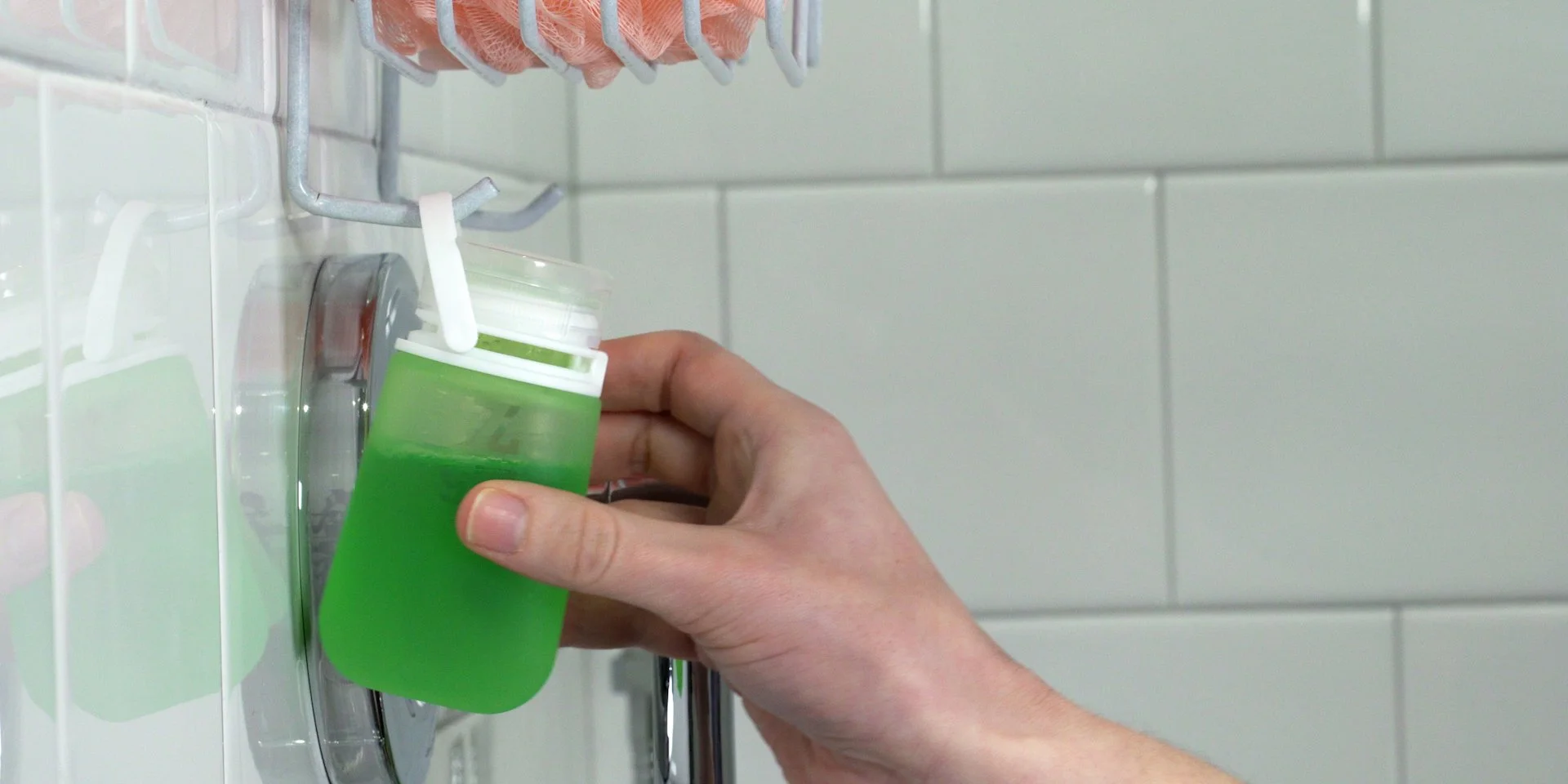 Person attaching or removing a green liquid soap dispenser in a shower setting.