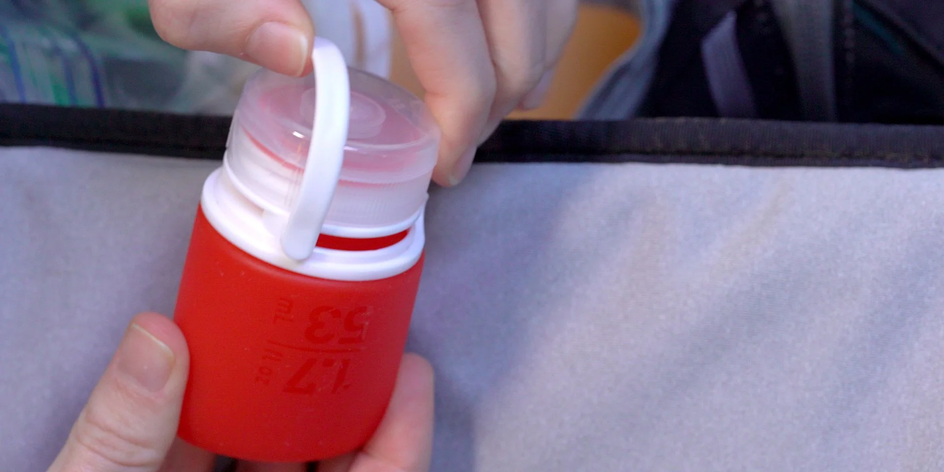 Person holding a red silicone travel bottle with a white lid and hook.