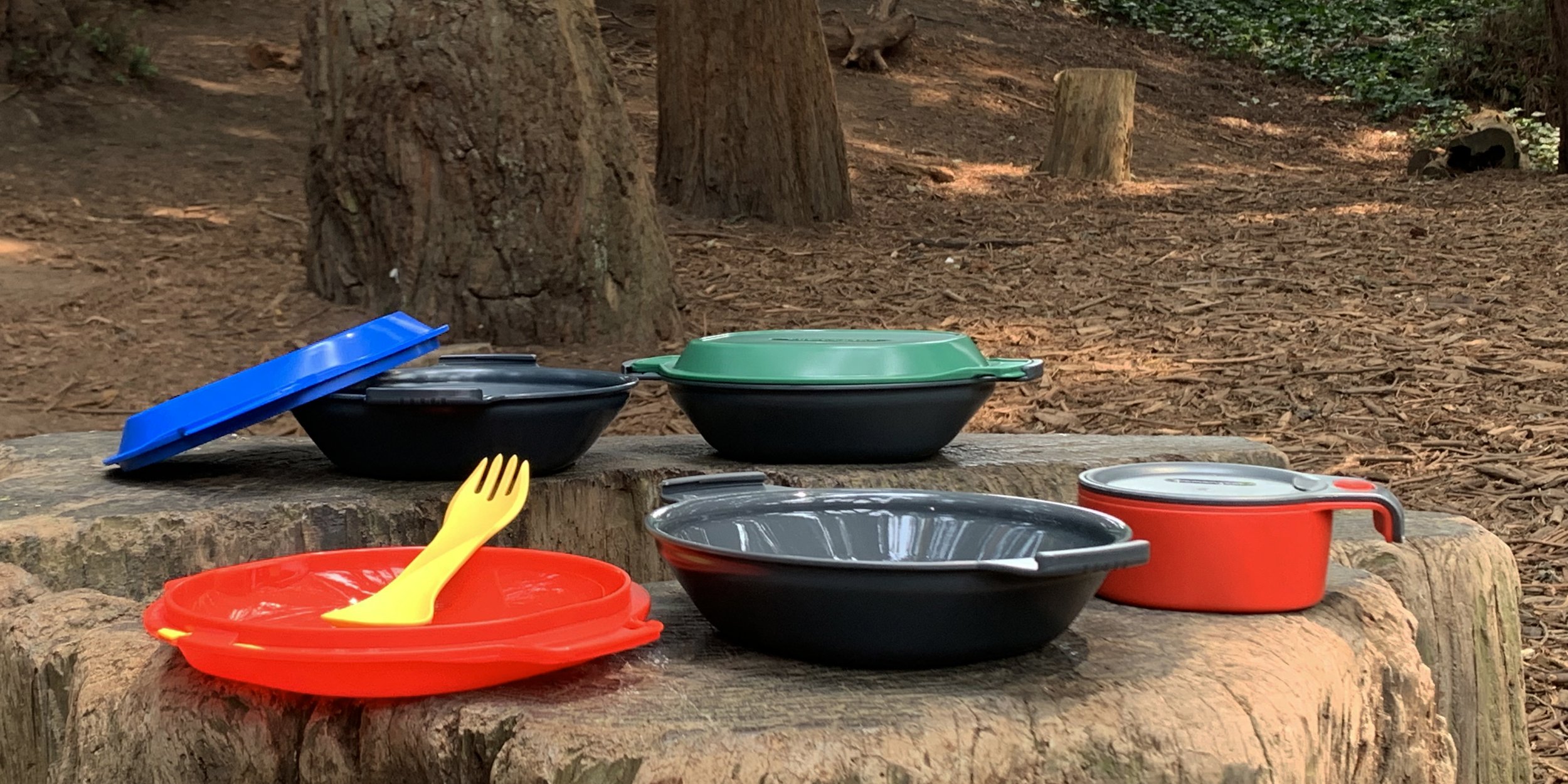 Camping cookware set with colorful lids on a wooden surface outdoors