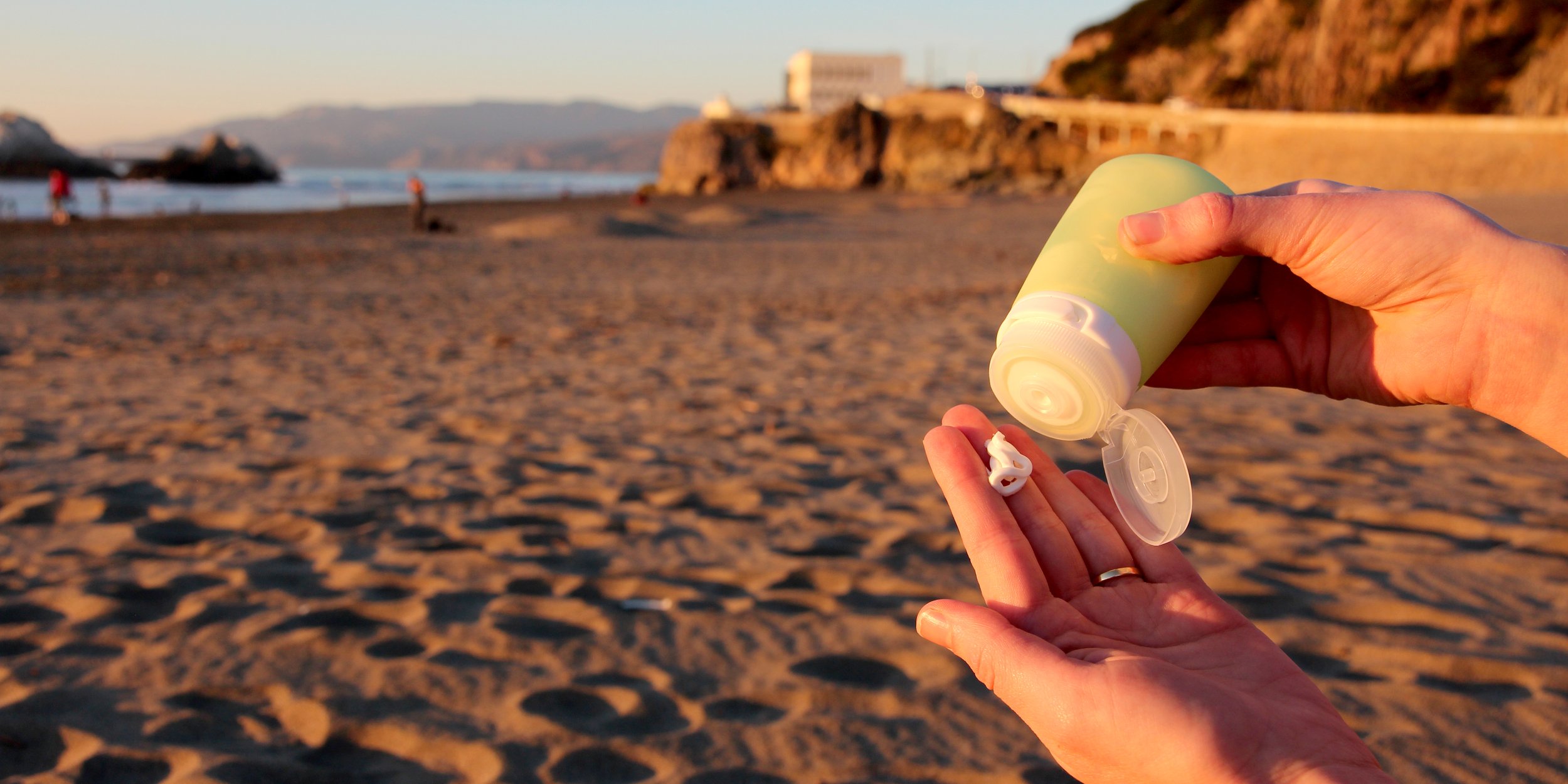 Person applying sunscreen at a sandy beach during sunset.