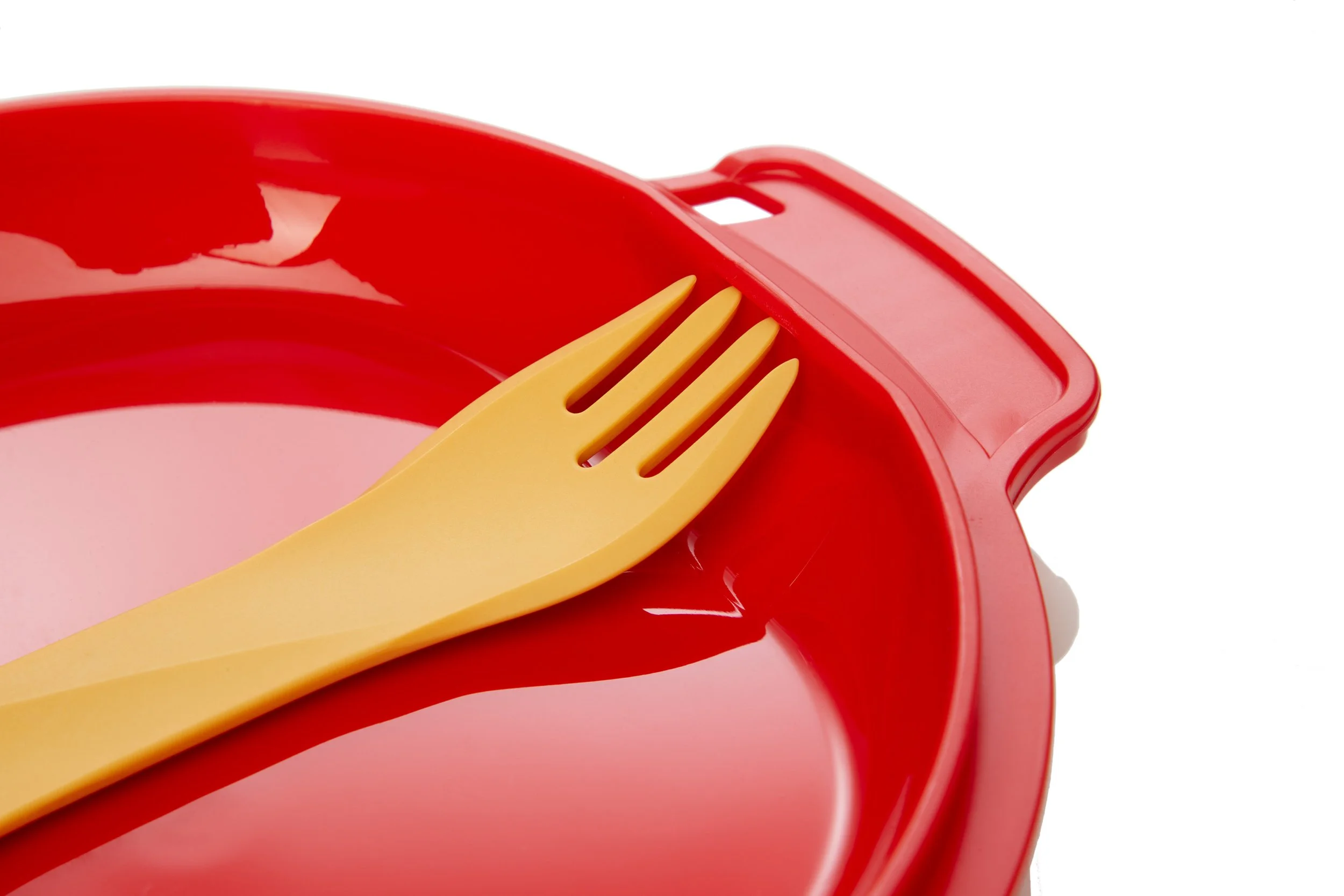 Yellow plastic spork on a red plate with a handle.