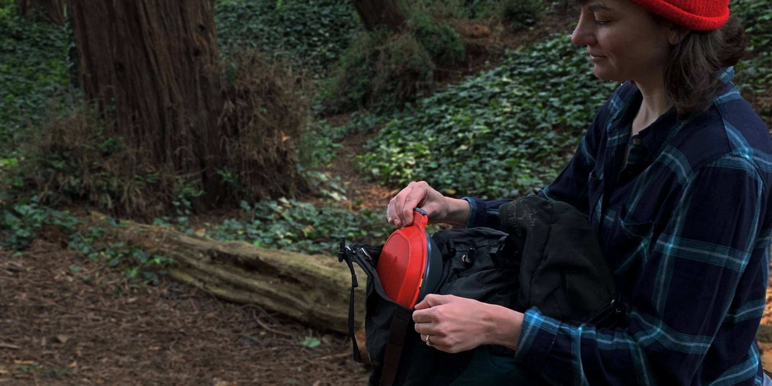 Person in red beanie holding a red object in a forest