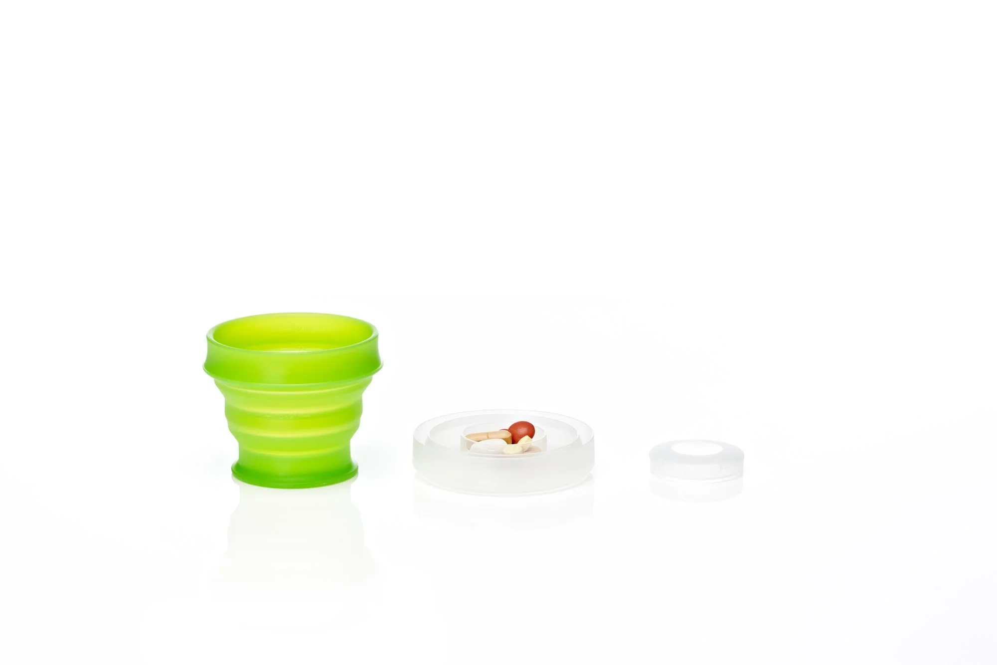 Collapsible green cup with a white container holding pills on a white background.