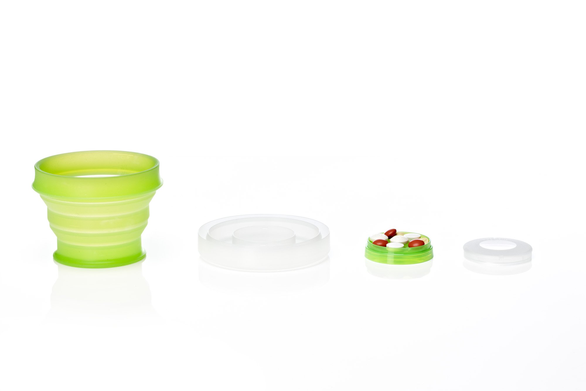 Collapsible green silicone cup and container lid with assorted pills on white surface.