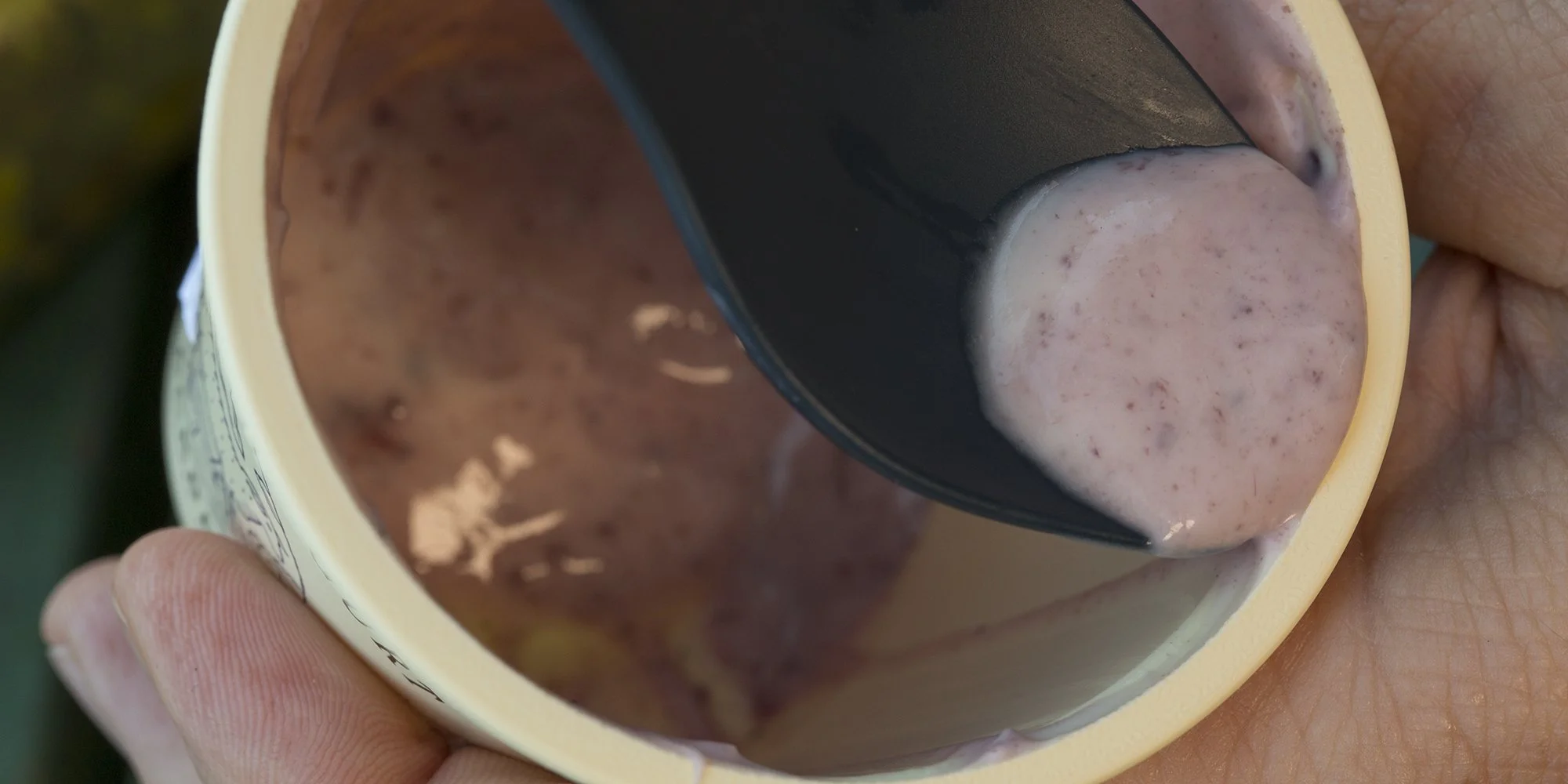 Close-up of a yogurt cup being held, with a spoon scooping up creamy, pink yogurt.