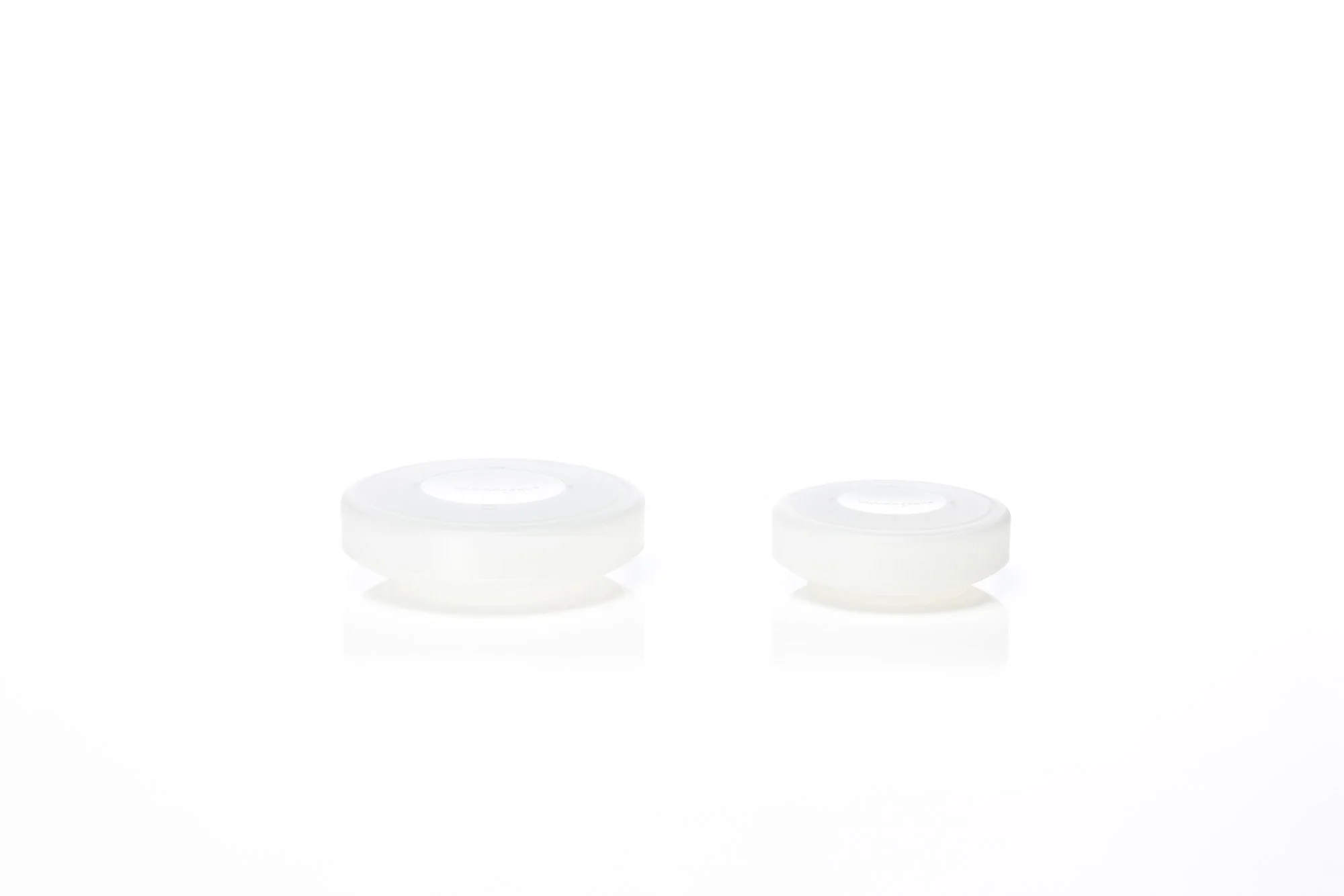 Two transparent round containers with white lids on a white background