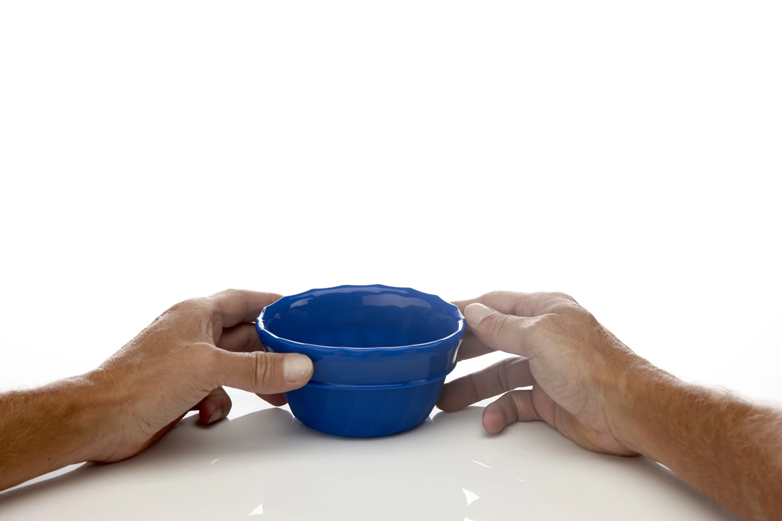 Hands holding a small blue bowl on a white surface.