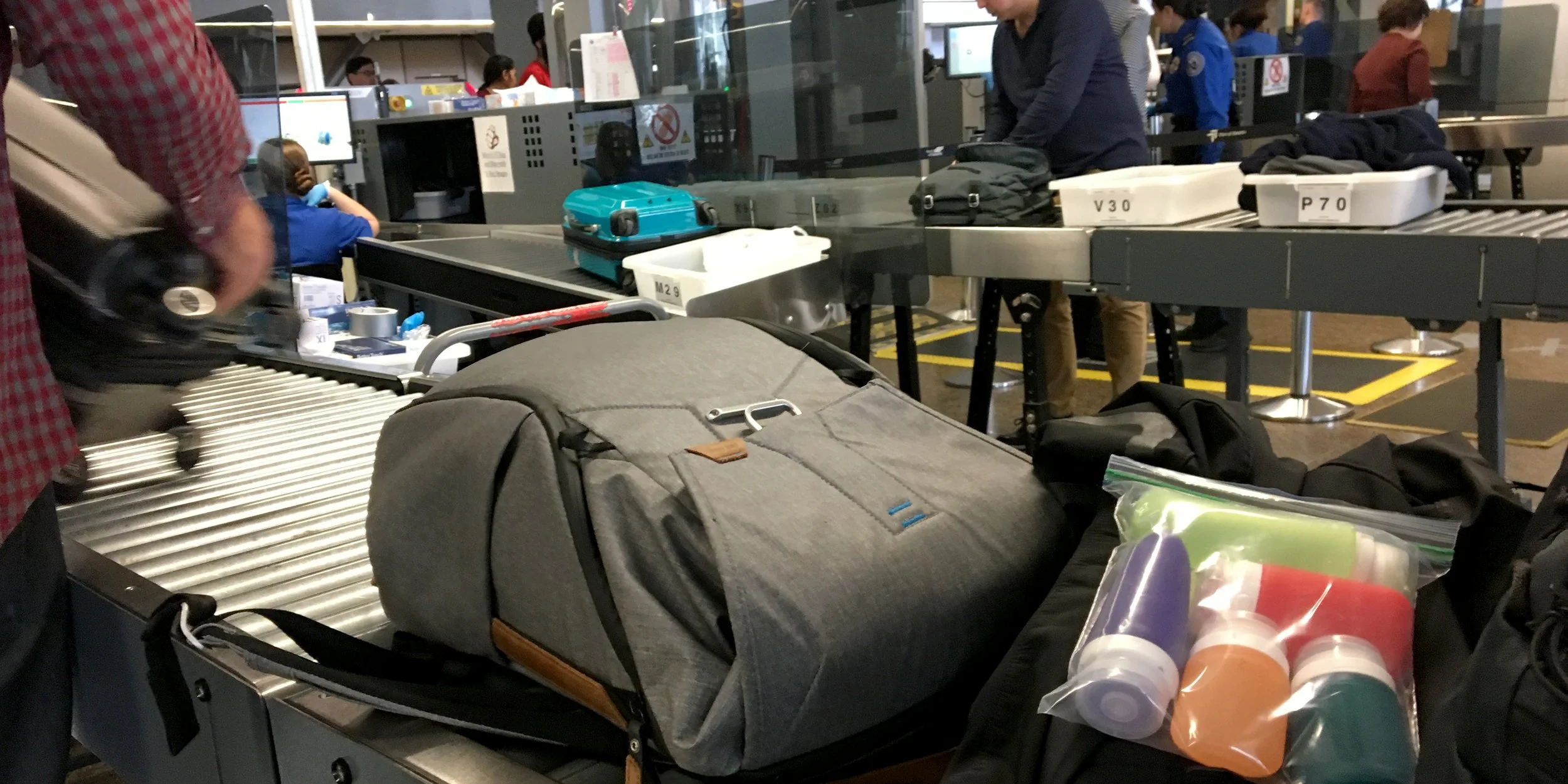 Airport security checkpoint with luggage and containers on conveyor belt.