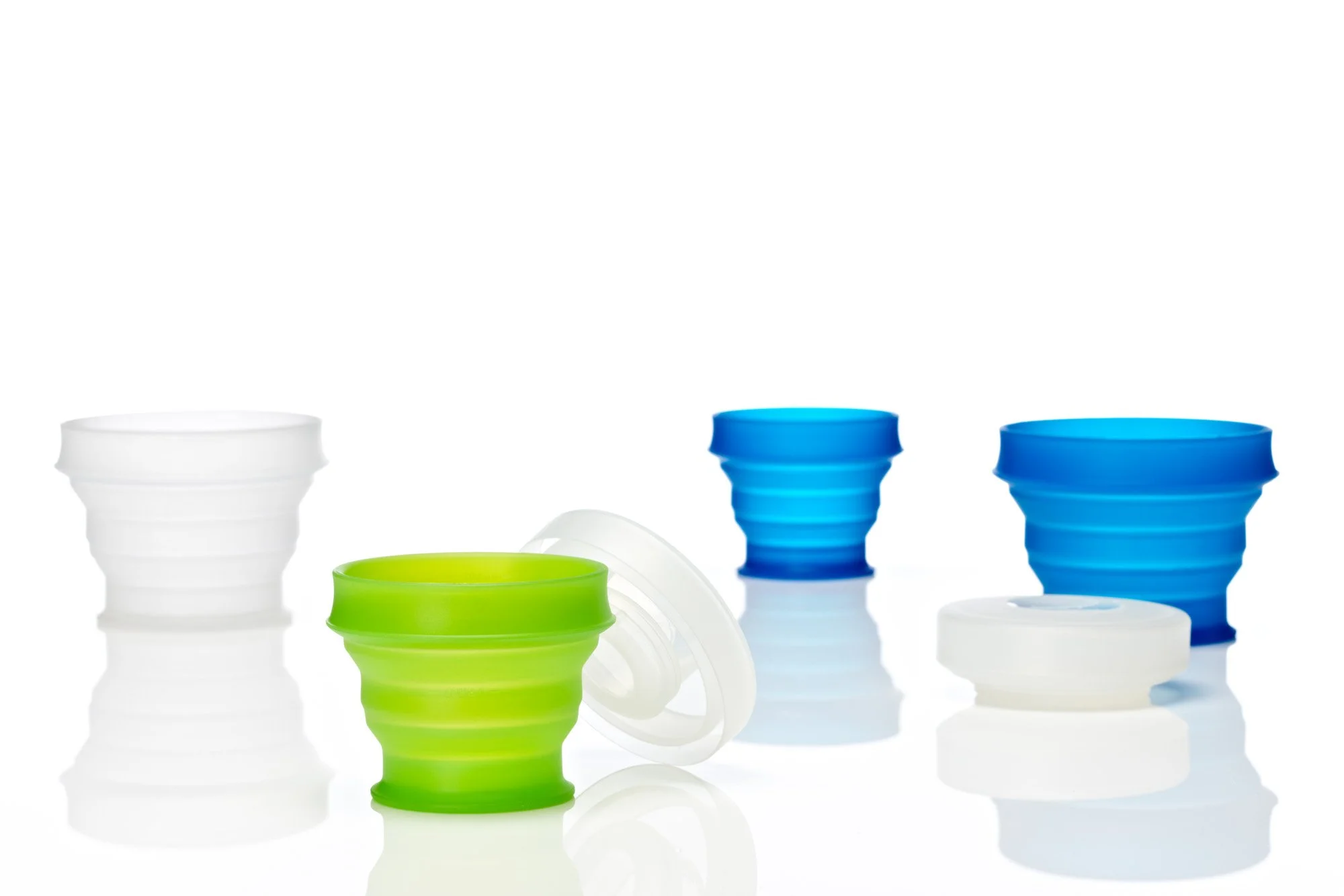 Collapsible silicone cups in green, blue, and white on a reflective surface.