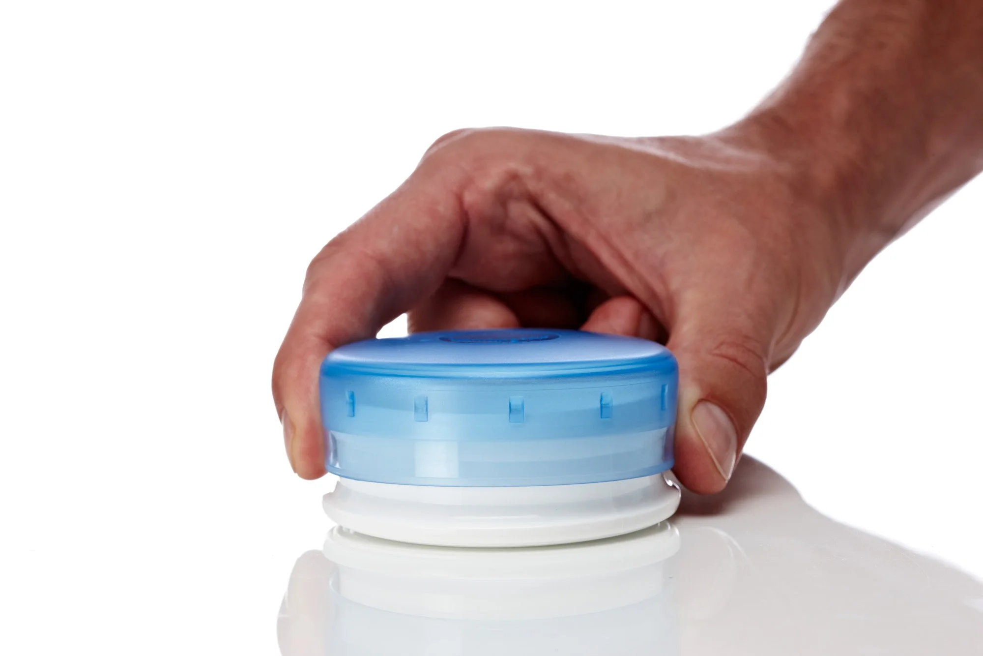 Hand pressing a blue button-like object on a white surface.