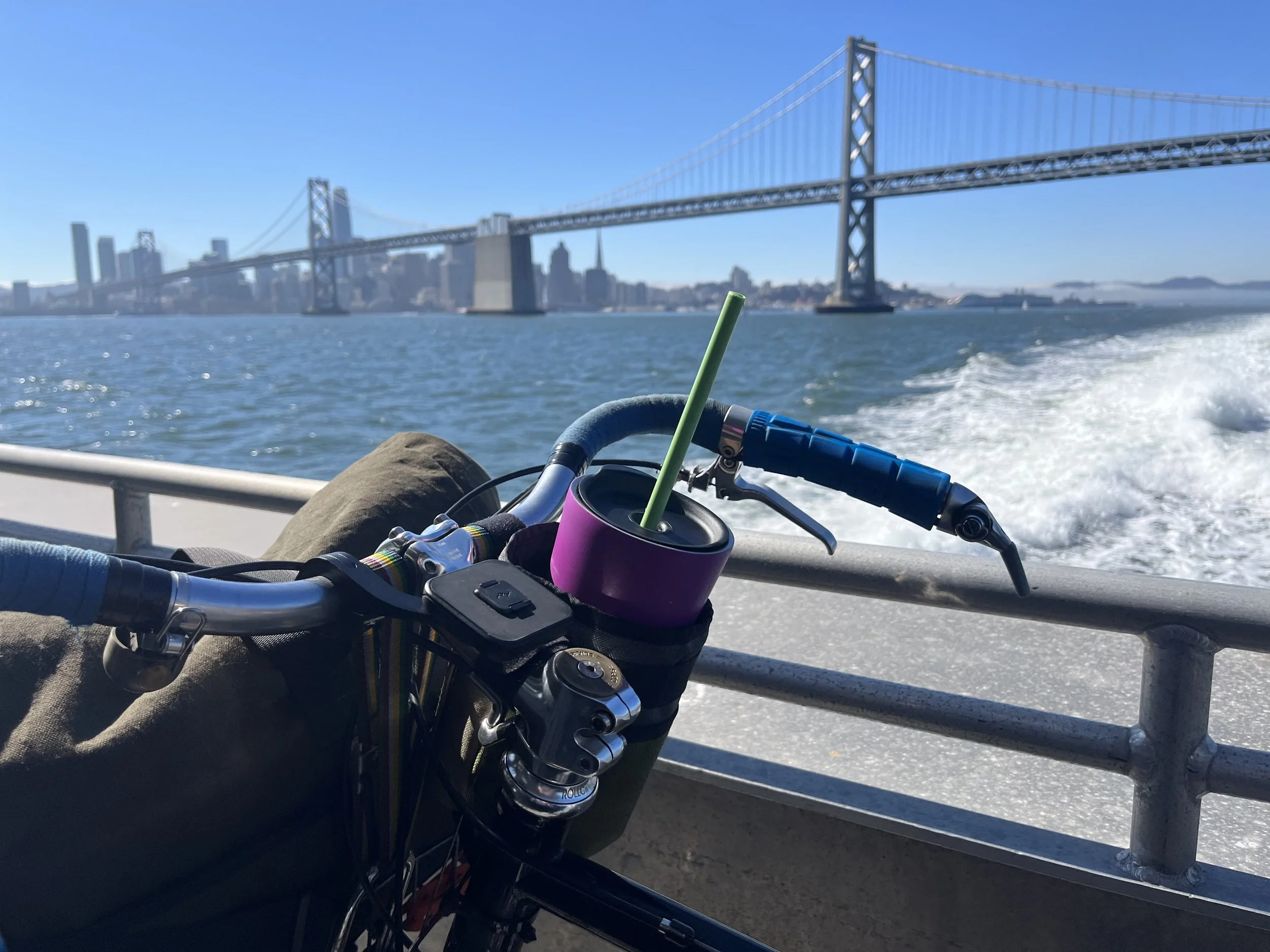 Bicycle handlebars and drink holder on a ferry with the San Francisco Bay Bridge in the background.