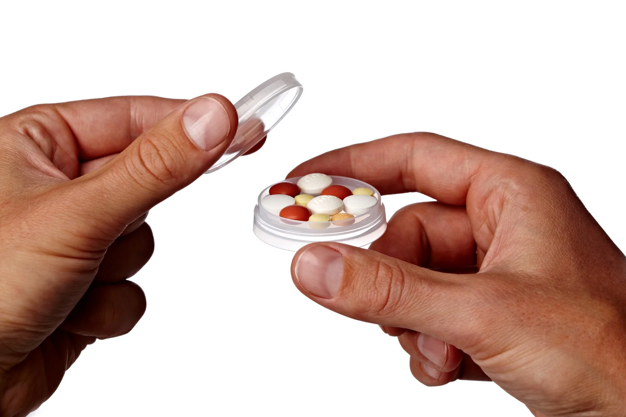 Hands holding a clear container with assorted pills on a white background.