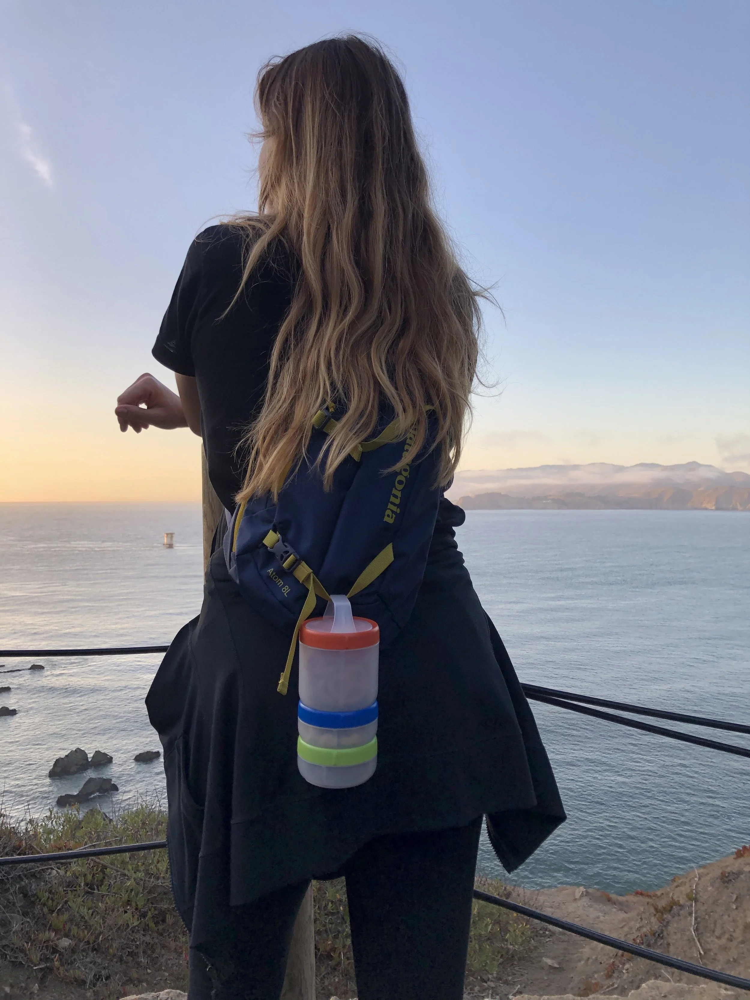Person overlooking ocean with backpack, containers, and sunset view.