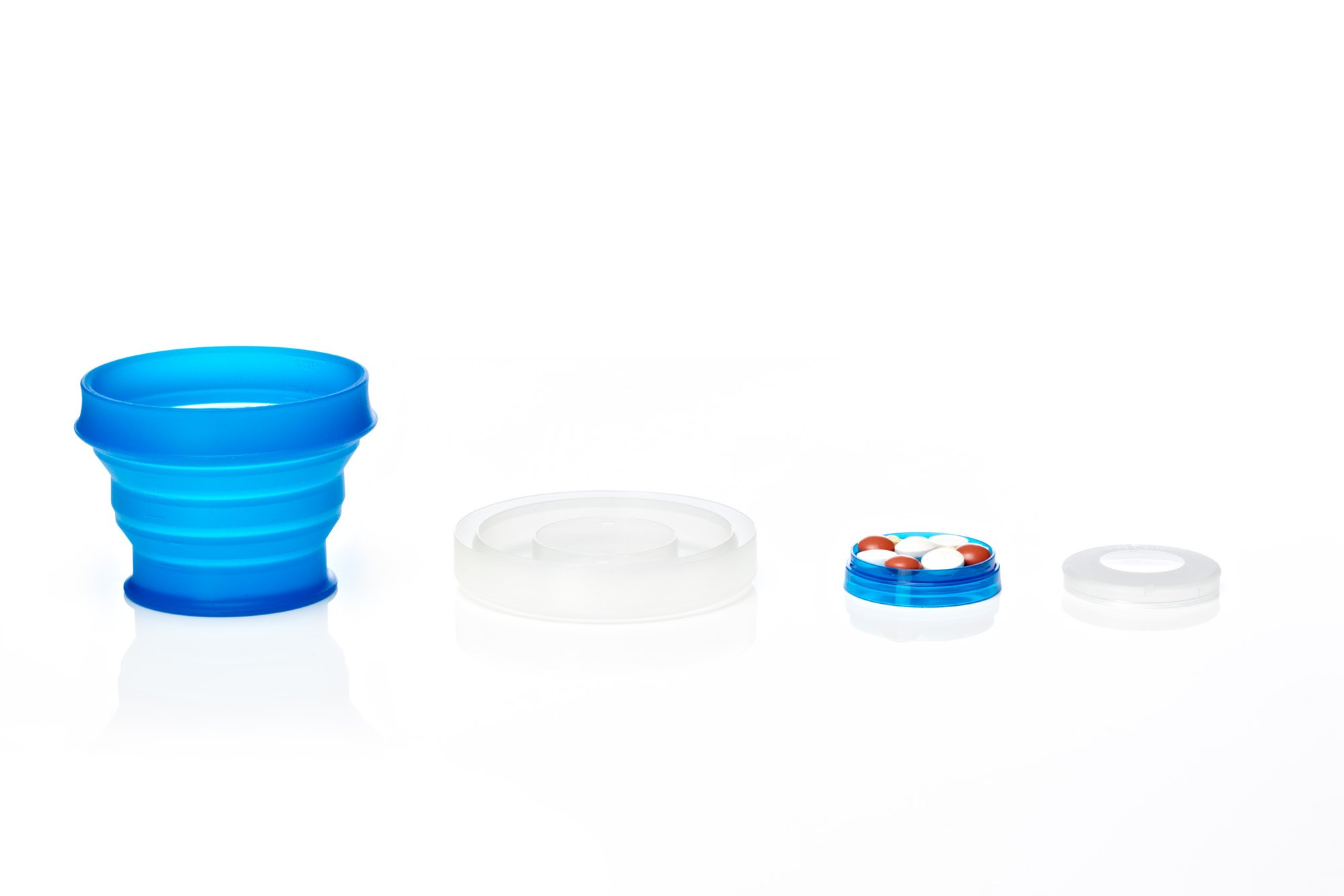 Collapsible blue silicone cup, white lid, compact pill organizer with pills, and clear plastic cap on a reflective surface.