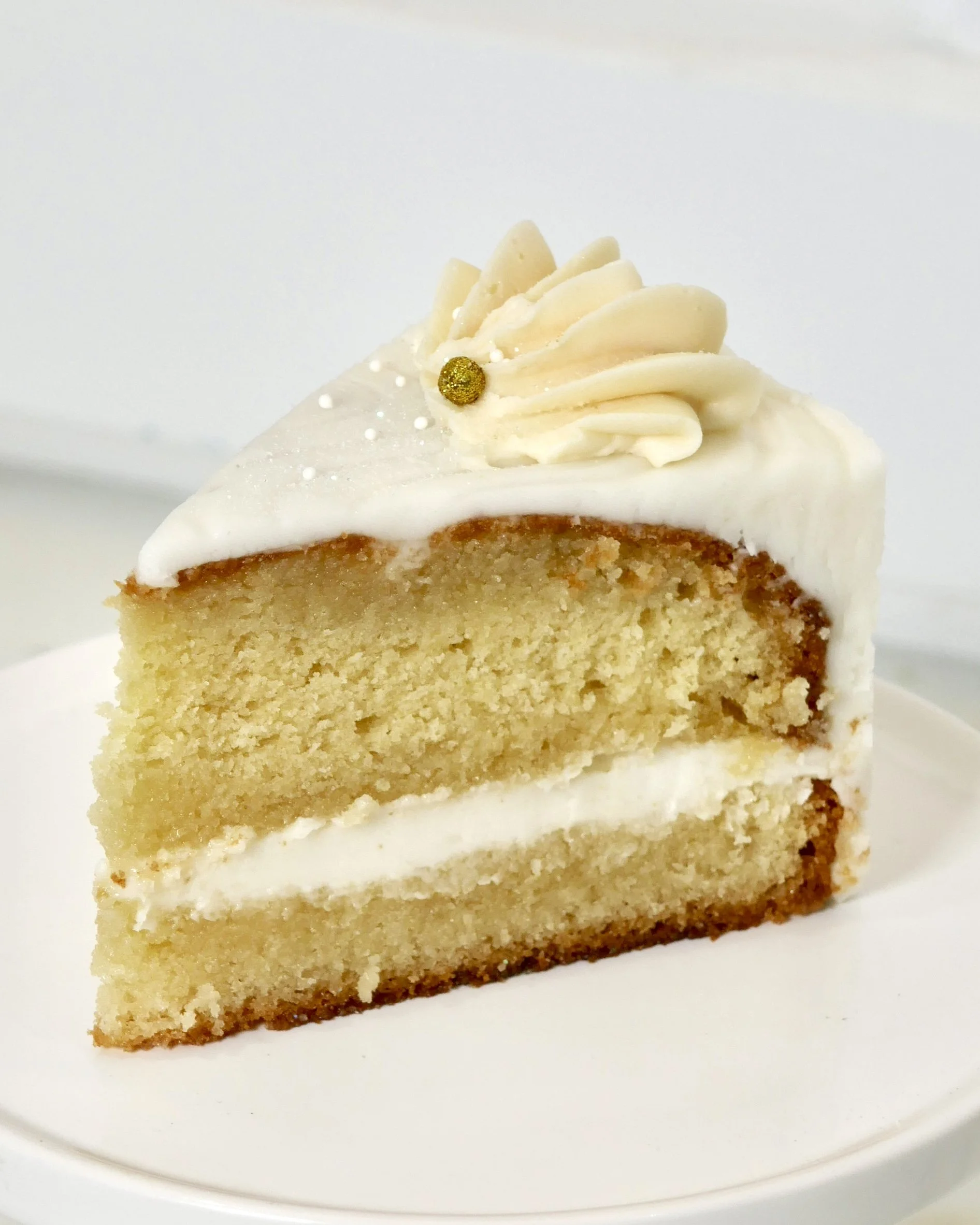 Close-up of a moist vanilla rum cake slice layered with rum-infused vanilla buttercream frosting, topped with decorative piping and a gold pearl.