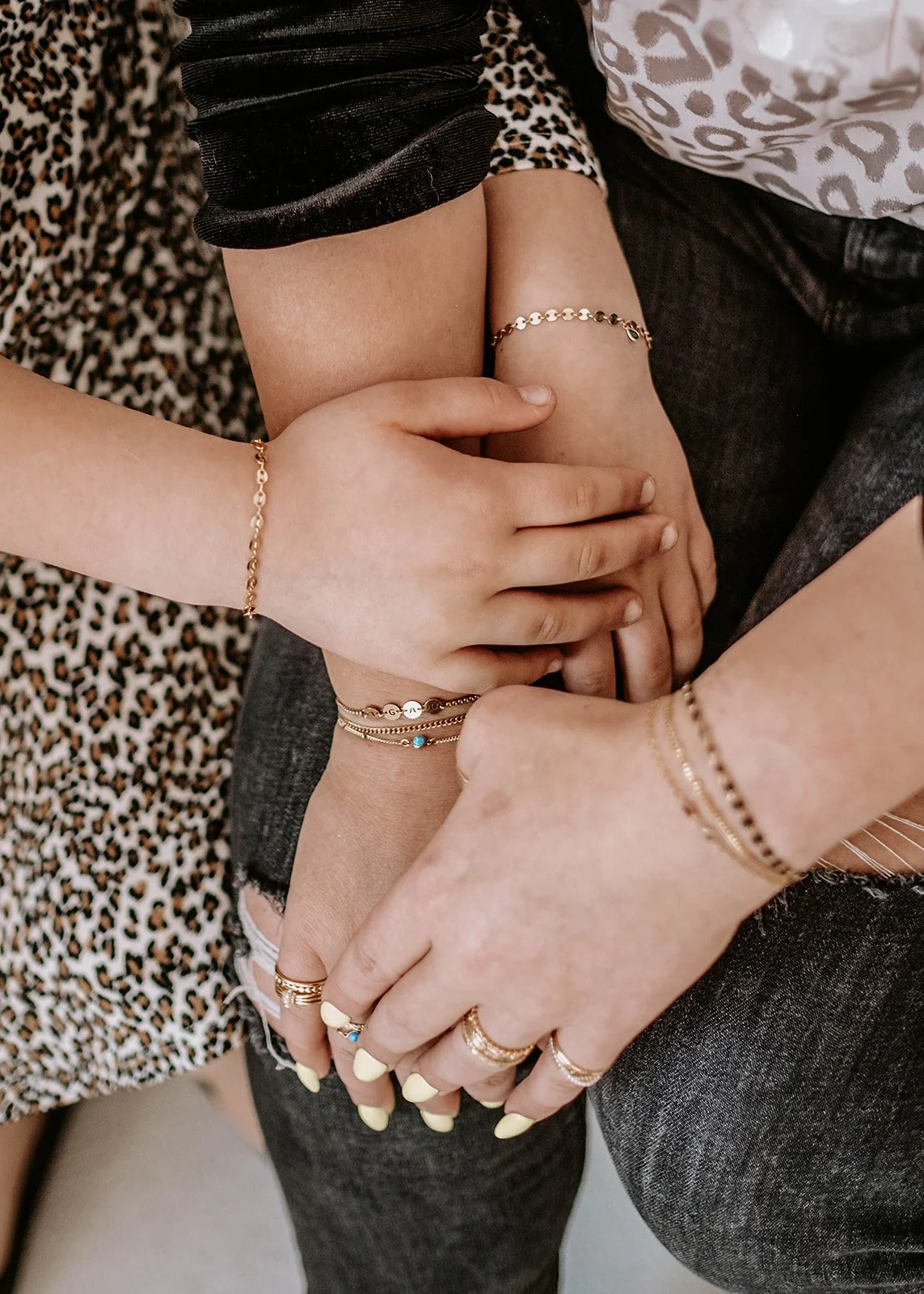 Close-up of three arms adorned with gold bracelets and rings. Two people are wearing animal print clothing and one has dark jeans.