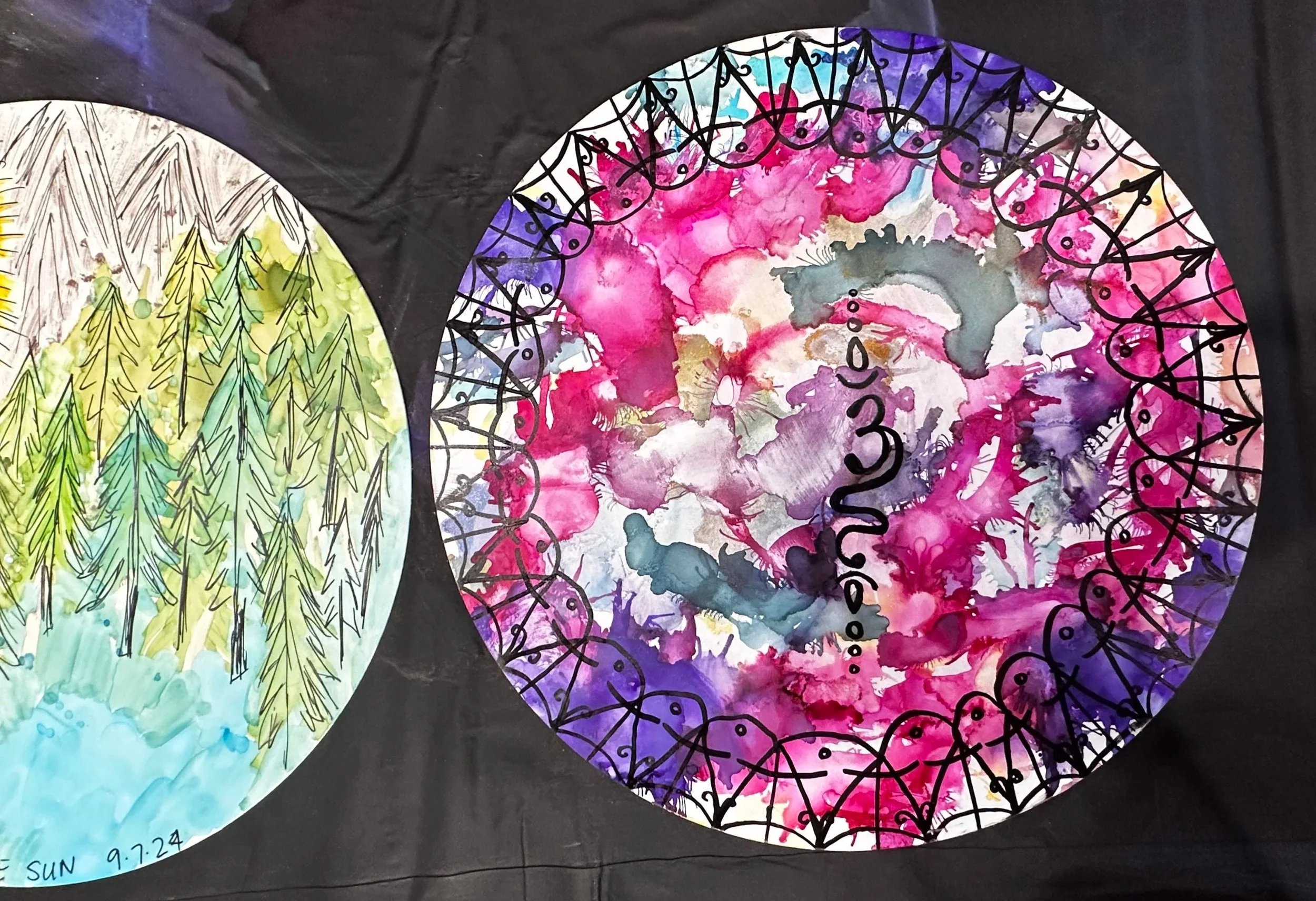 Two watercolor paintings, one with green pine trees and a blue sky, and the other with blended pink, purple, and gray colors, both within circular shapes on a black background.