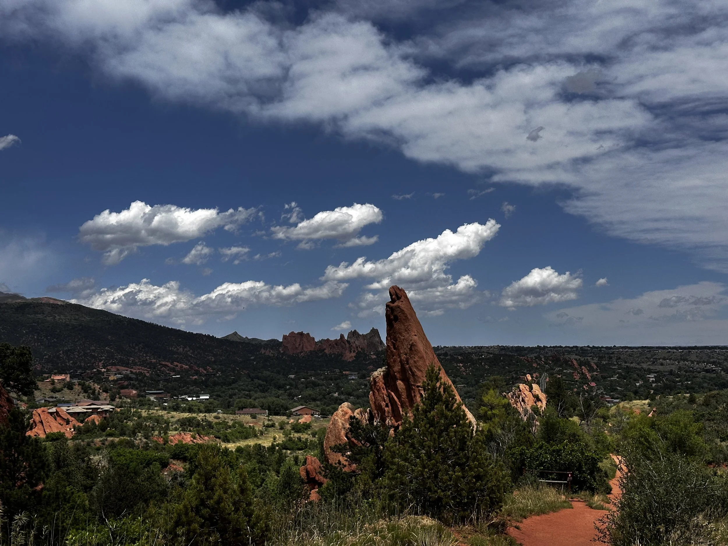 Scenic view of rock formations, green trees, and a small town in the valley under a partly cloudy sky.