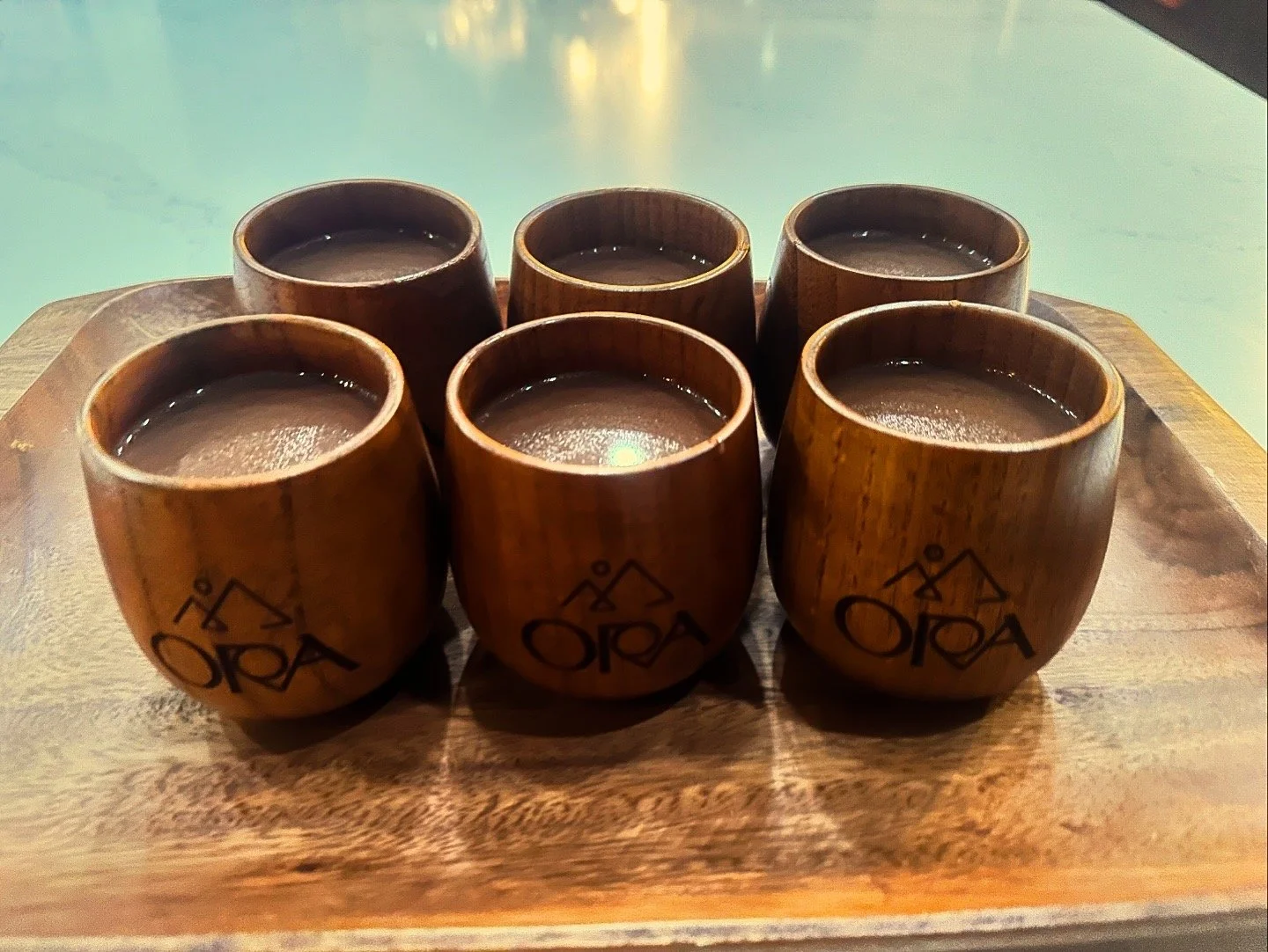 Six small wooden cups with hot beverages on a wooden tray