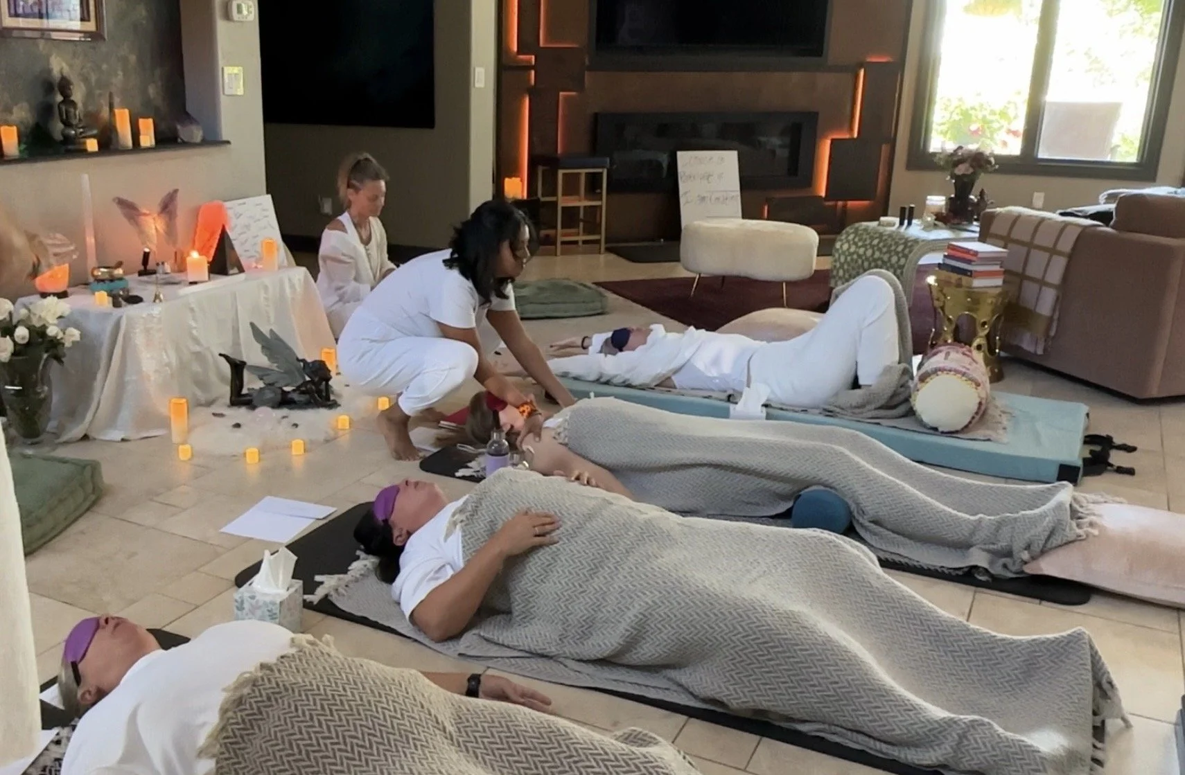 People practicing yoga or meditation in a living room with candles, flowers, and spiritual decor.
