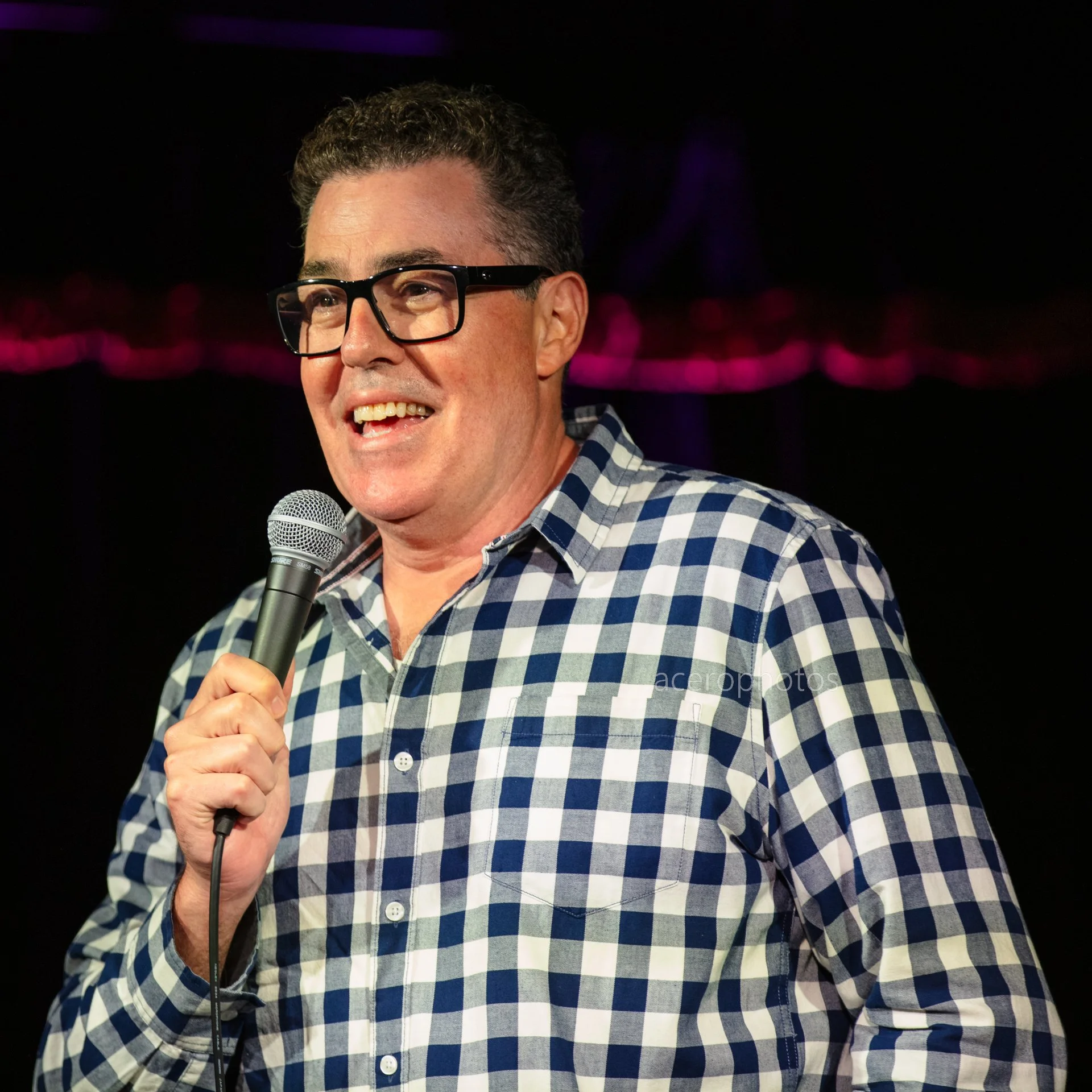 acerophotos-adam-carolla-on-stage-with-a-microphone-wearing-stripped-white-blue-shirt-acero-photos.jpg