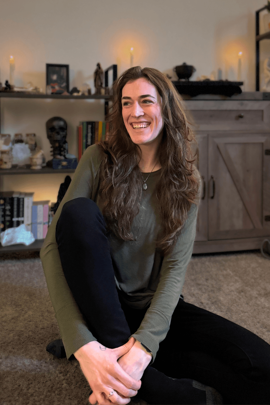 Ariel smiling, and sitting cross-legged on the floor in black pants and a green shirt.