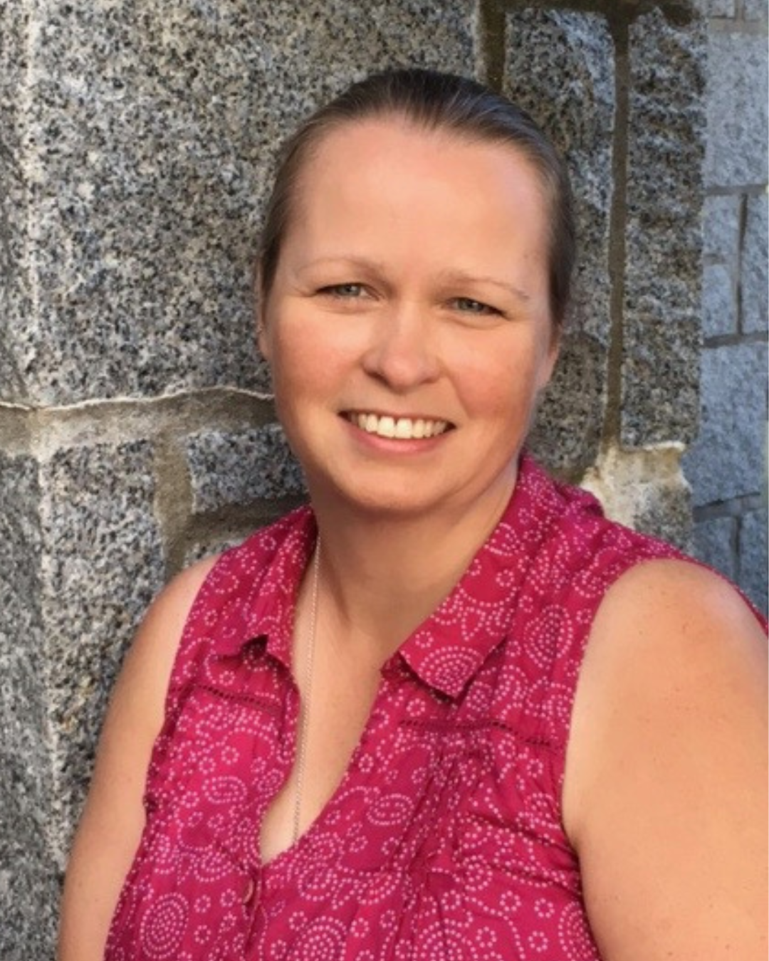 Picture of me in a pink, sleeveless shirt, against a brick wall.