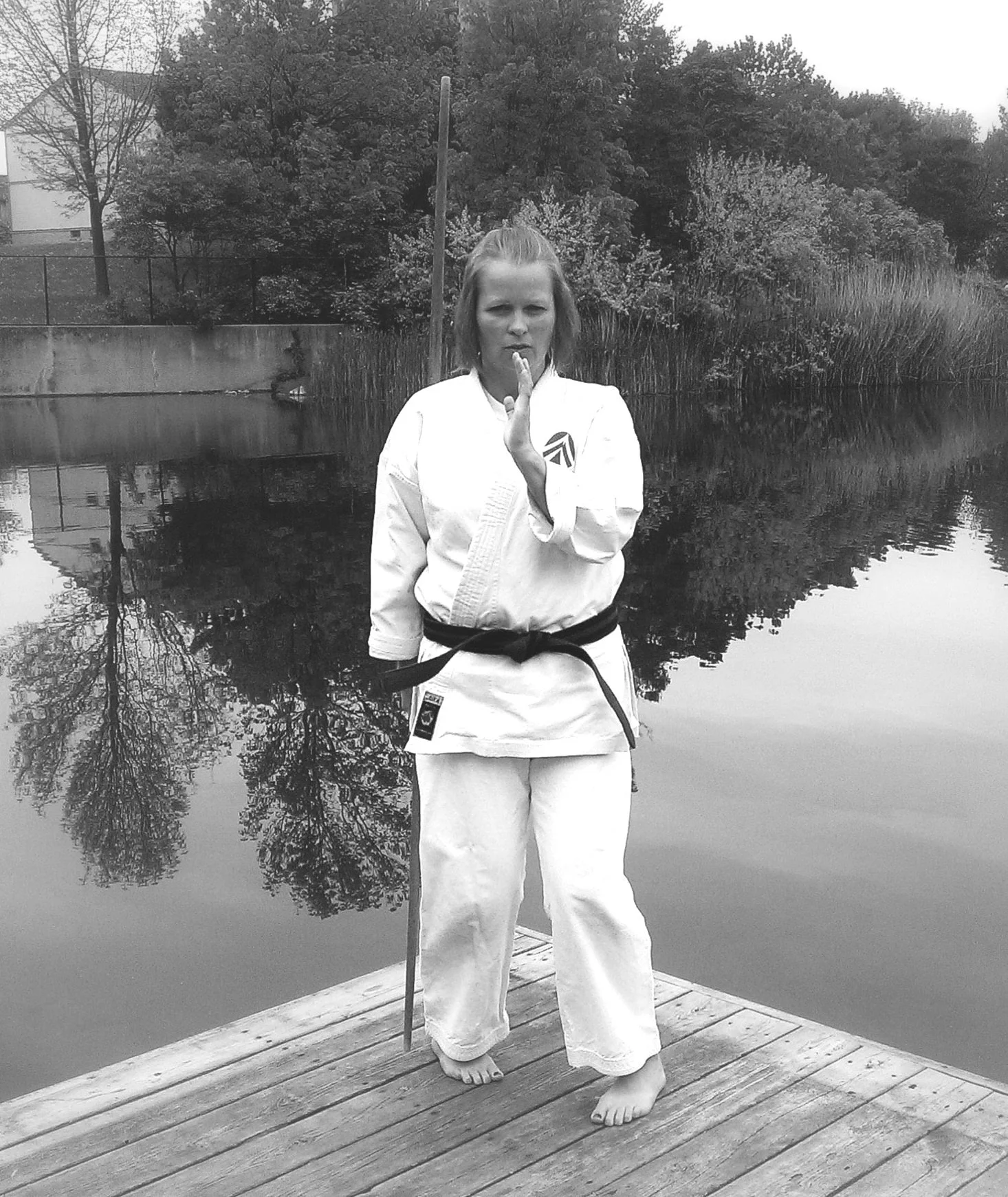 Picture of Heather Daun wearing a white karate uniform, with a black belt around her waist and posing in a karate stance with a bo, 6 foot staff.