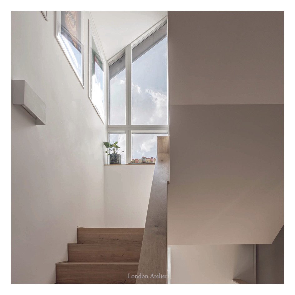 The staircase rises through the house to a roof-level window arrangement that acts as a lantern, drawing daylight deep into the interior. This vertical shaft of light transforms the stair into a sculptural element, guiding movement while softly illum