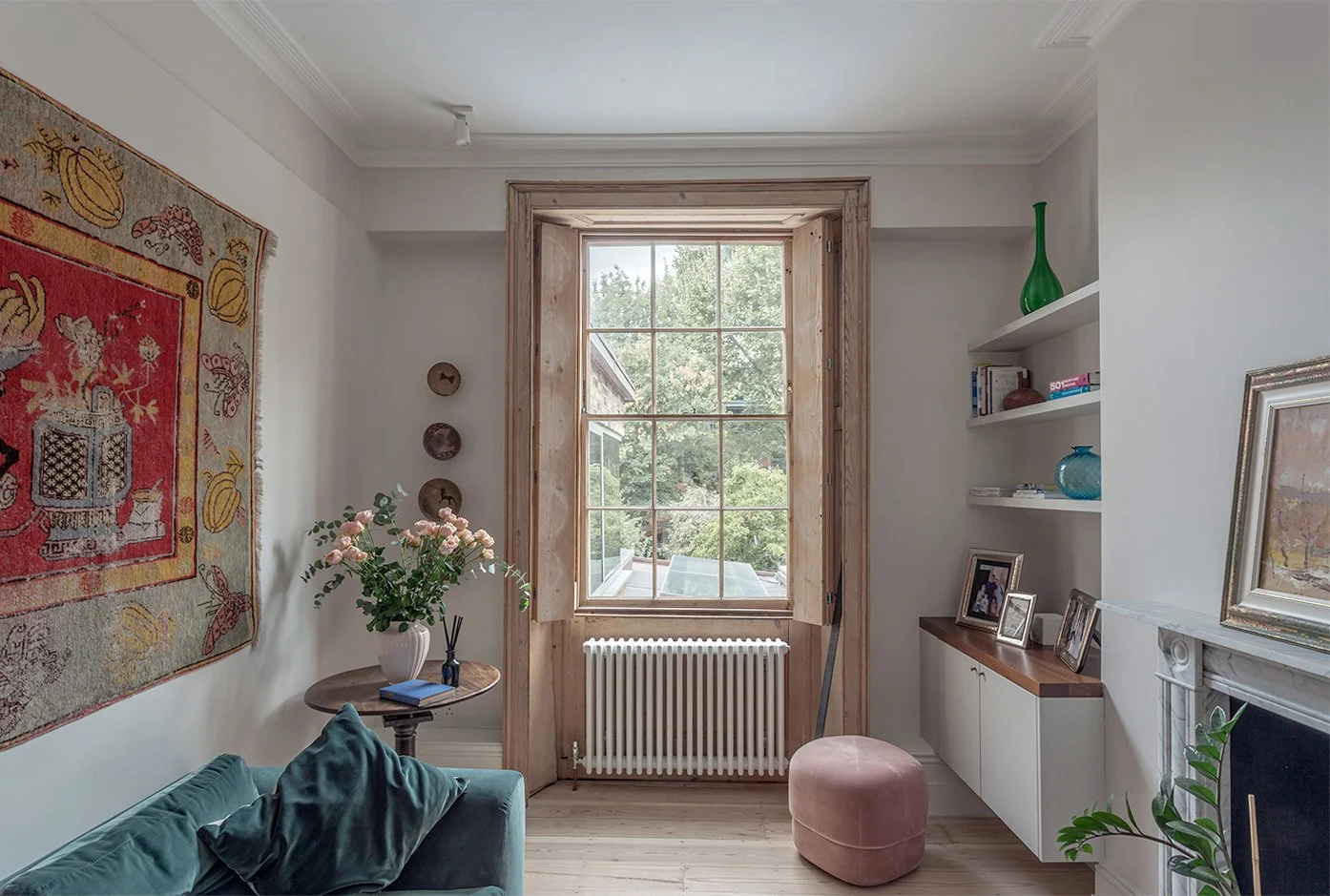 Living room with timber-framed sash window, built-in shelving and fireplace, looking out towards the garden and rear extension.