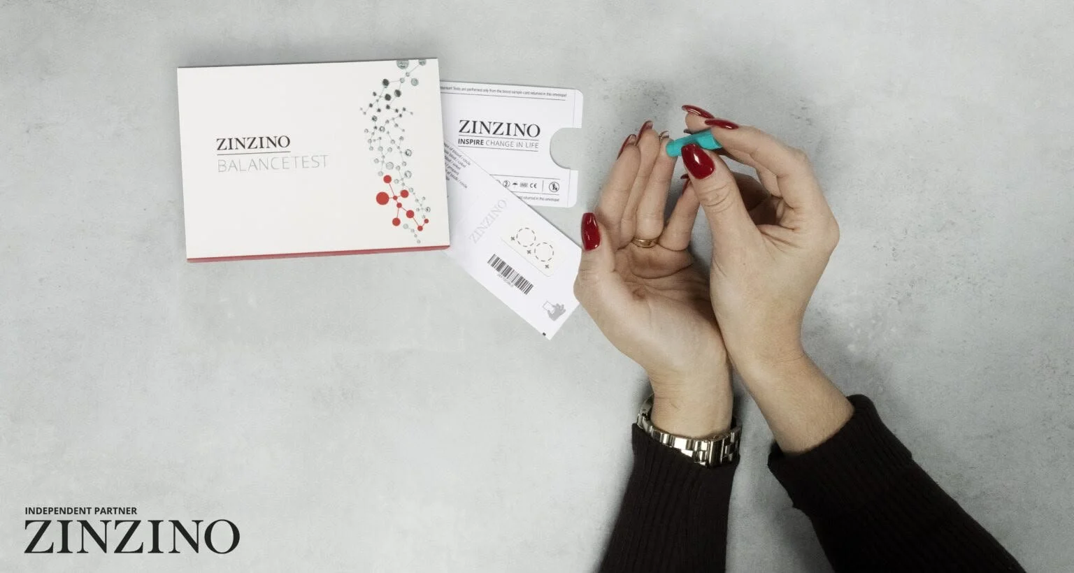 Person holding a test capsule above a testing kit from Zinzino, with the kit's packaging and paperwork on a gray surface.