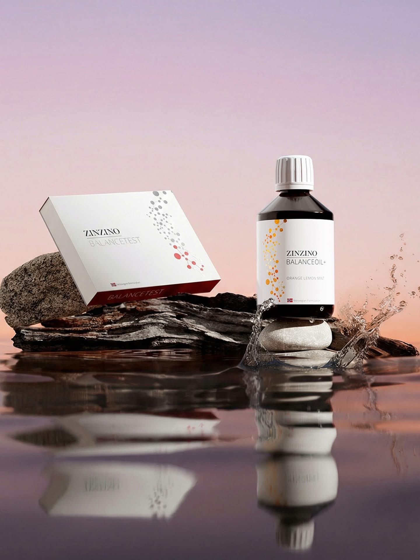 A bottle of Zinzino BalanceOil with orange lemon mint flavor on a rock, with a box of BalanceTest on the left, all set against a pinkish sky background with water reflecting the objects.
