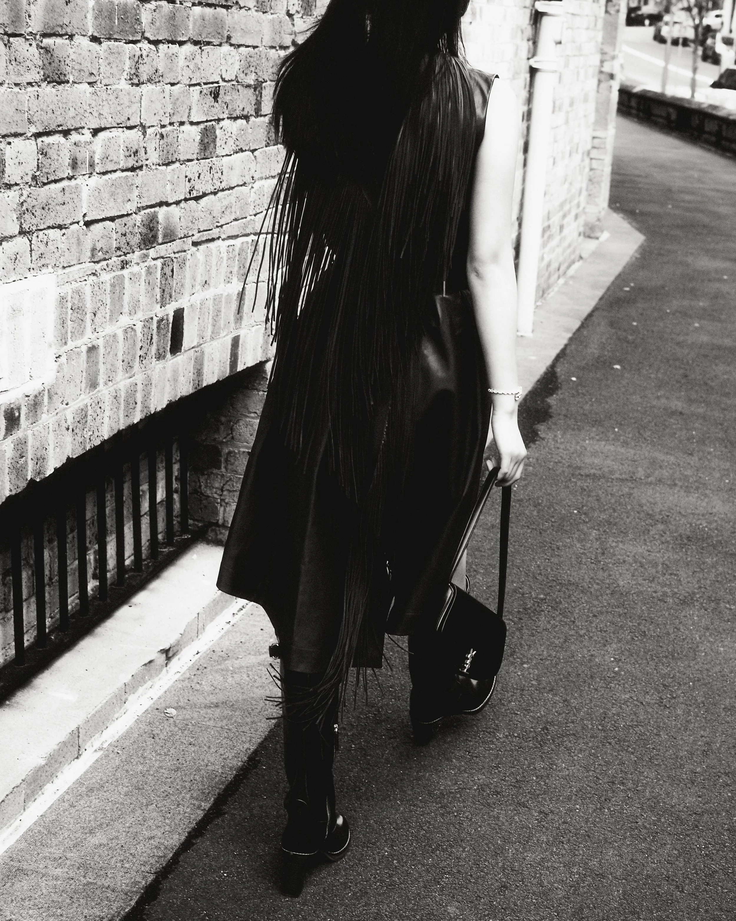 A black and white image of a woman with short hair and earrings, standing in front of a large poster of a woman with long hair and her eyes closed.