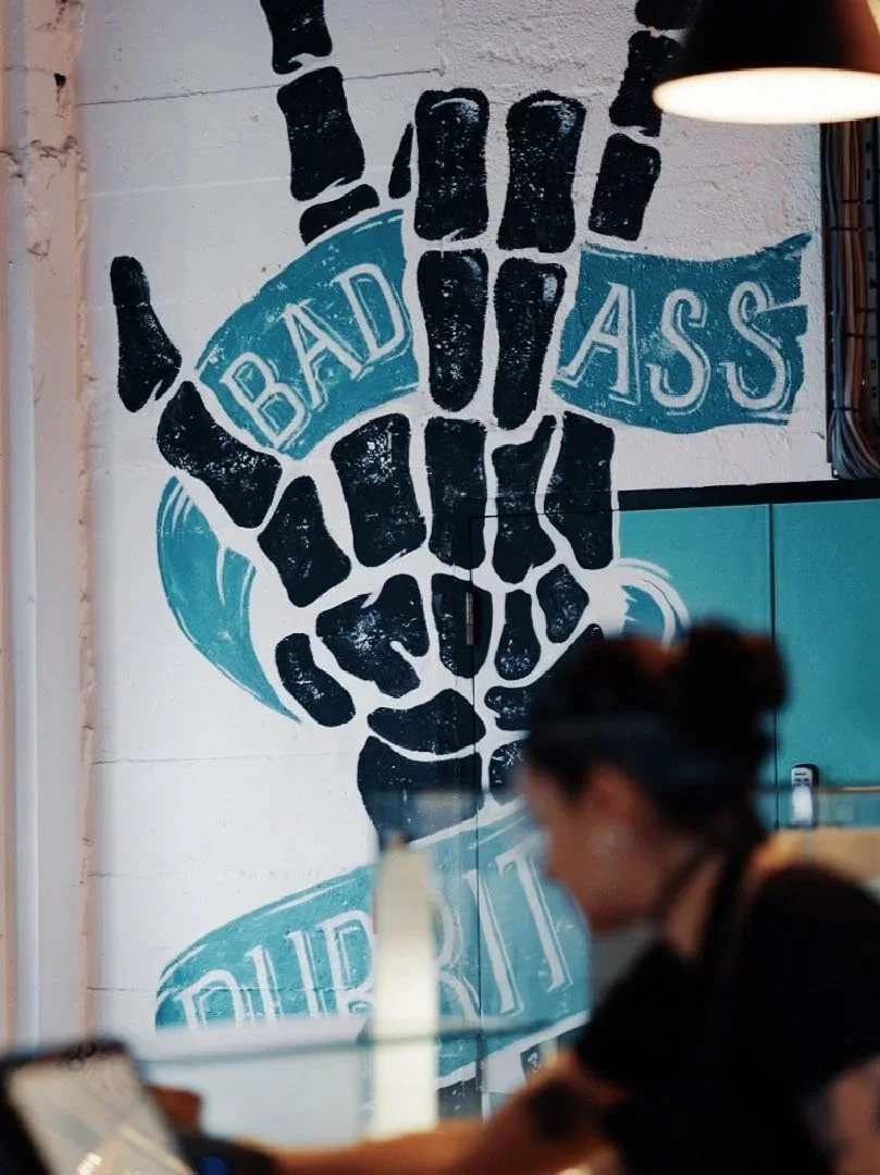 Wall art with a black fist holding a ribbon, with the words 'Bad Ass' written inside the ribbon.