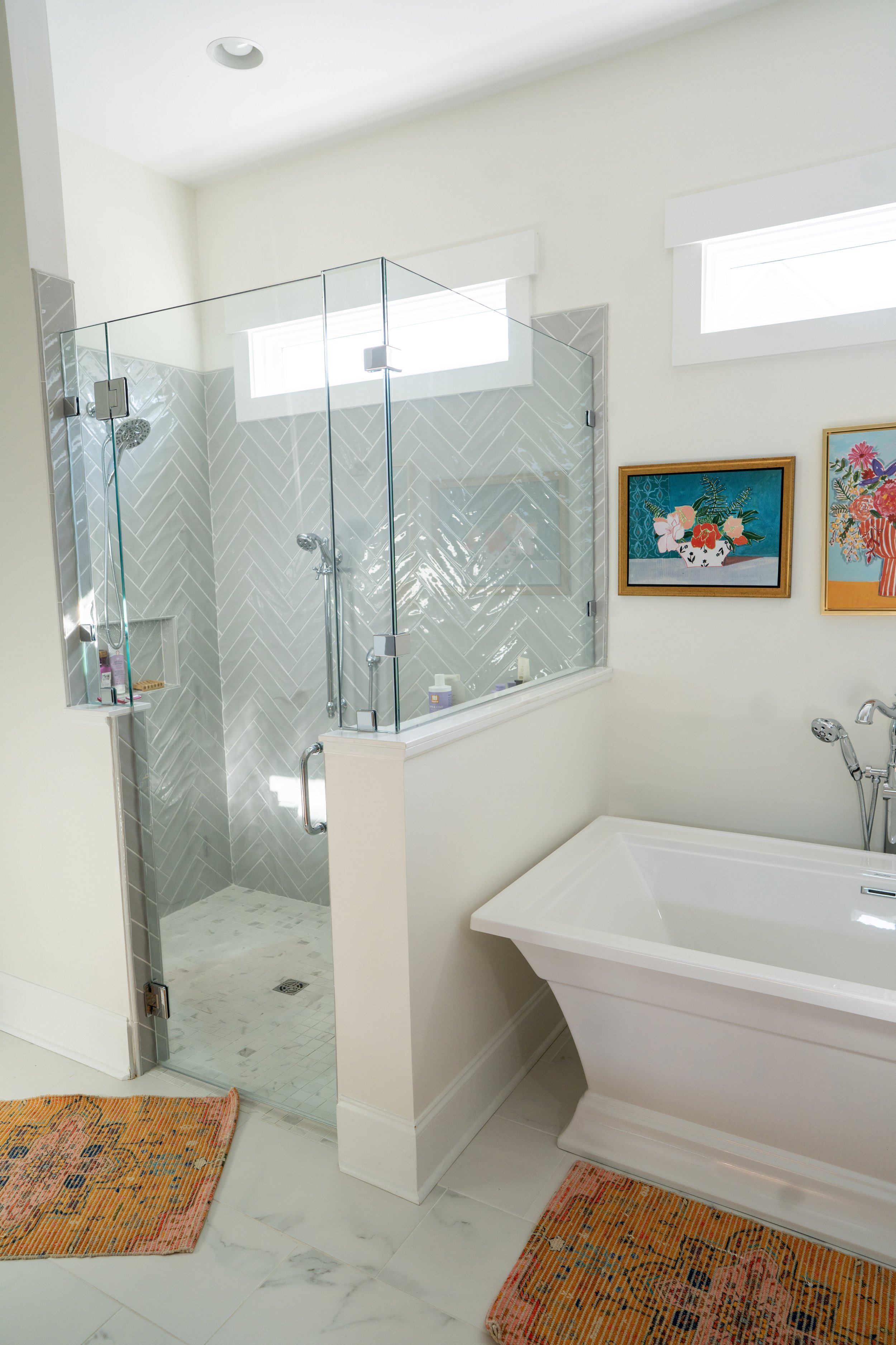Bathroom with a walk-in shower enclosed by glass, a white bathtub, and colorful framed artwork on the wall.