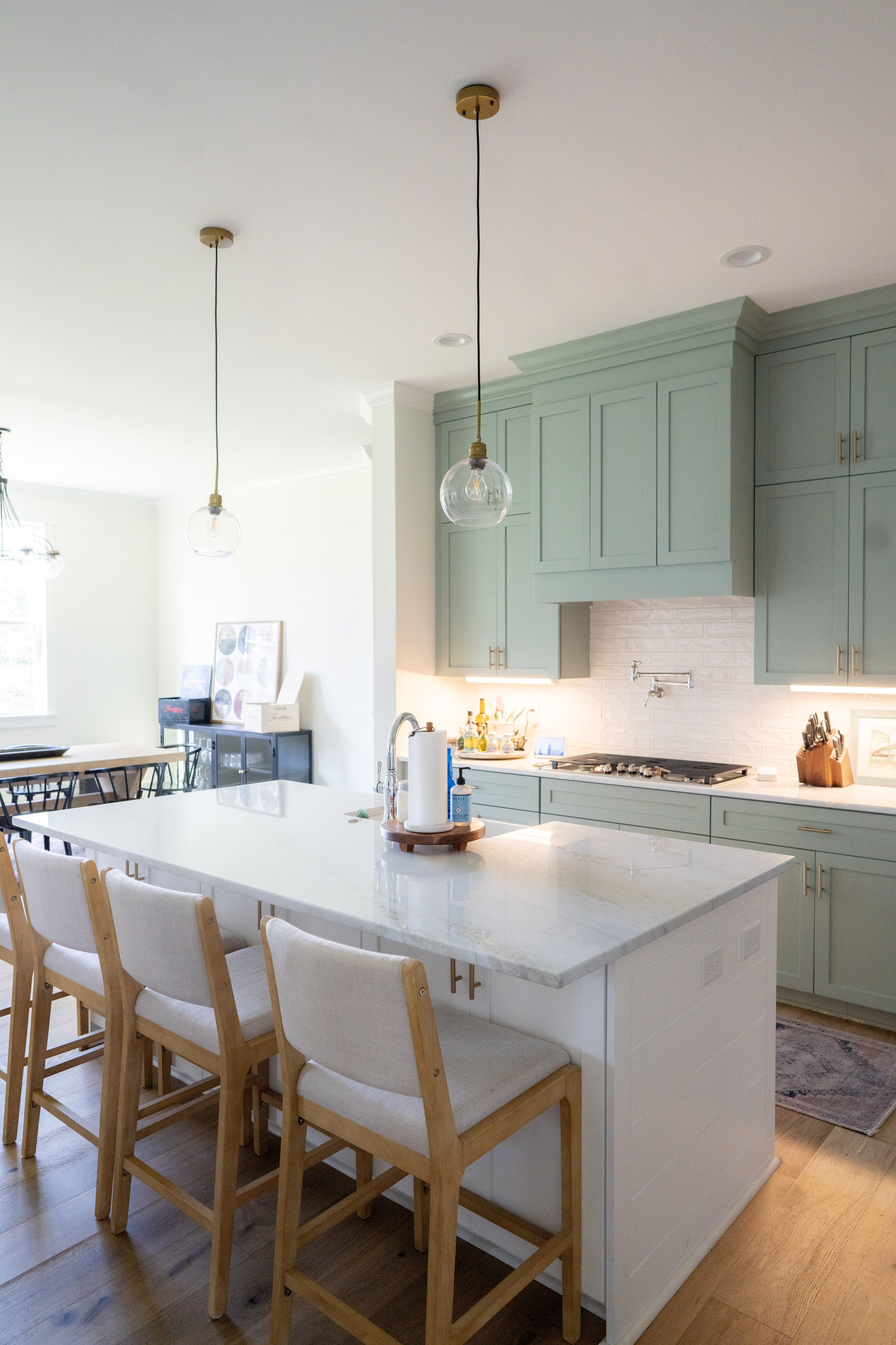 A modern kitchen with a white marble island, pale green cabinets, and pendant lights hanging from the ceiling.