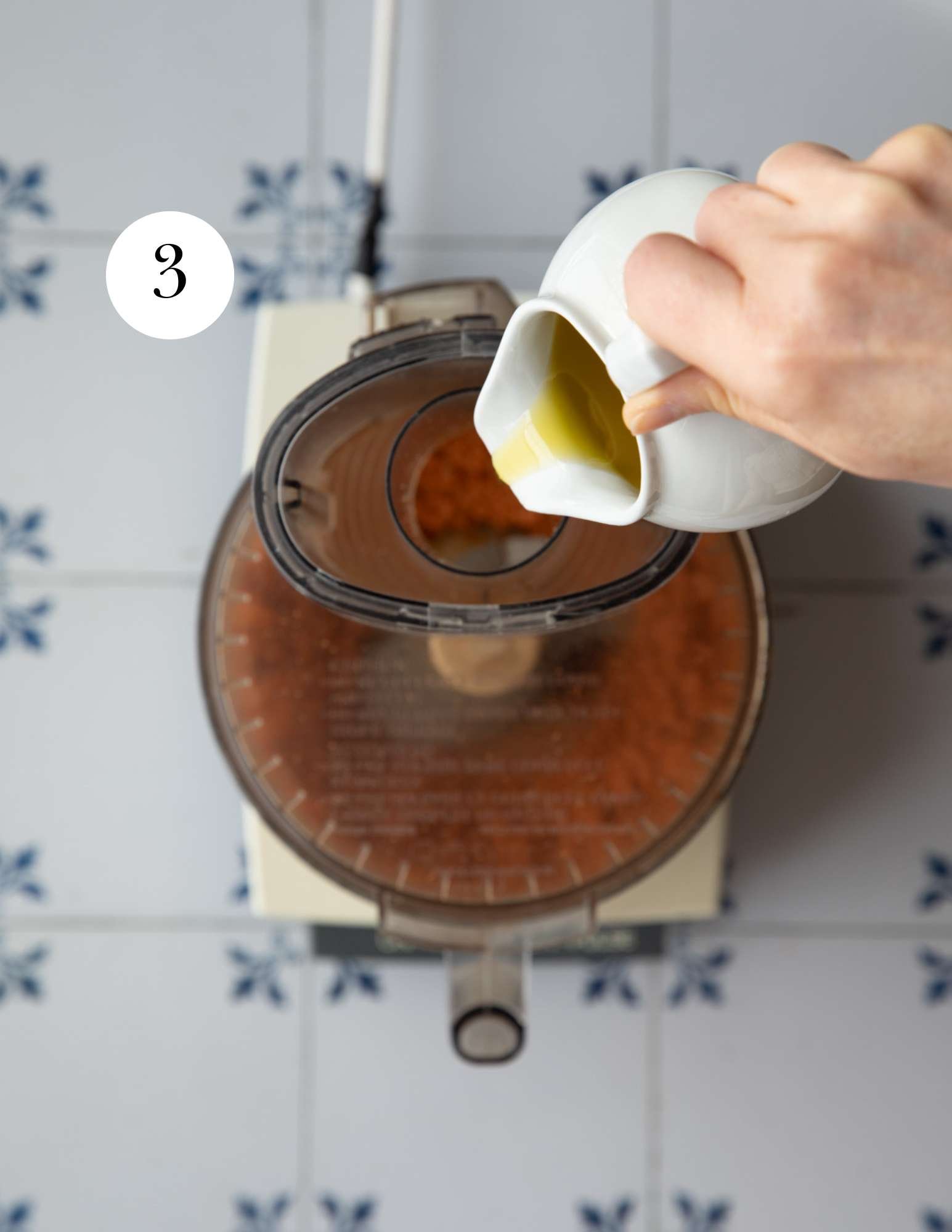 pouring olive oil into a food processor.
