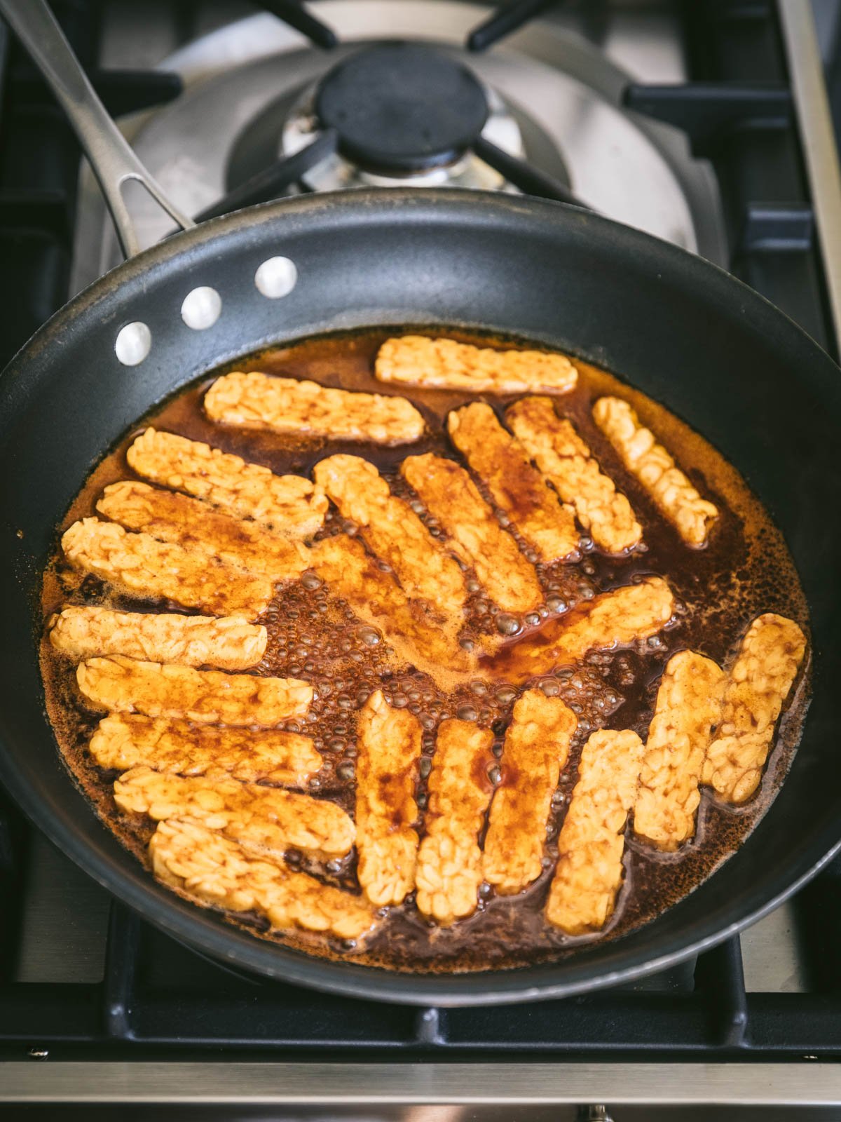 Tempeh bacon simmering on the stovetop