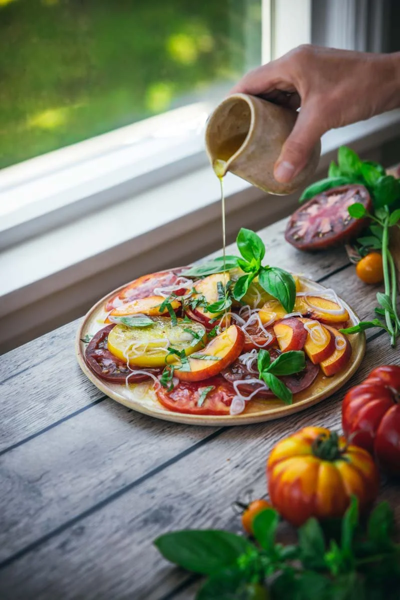 pouring orange vinaigrette over tomato crudo with stone fruit