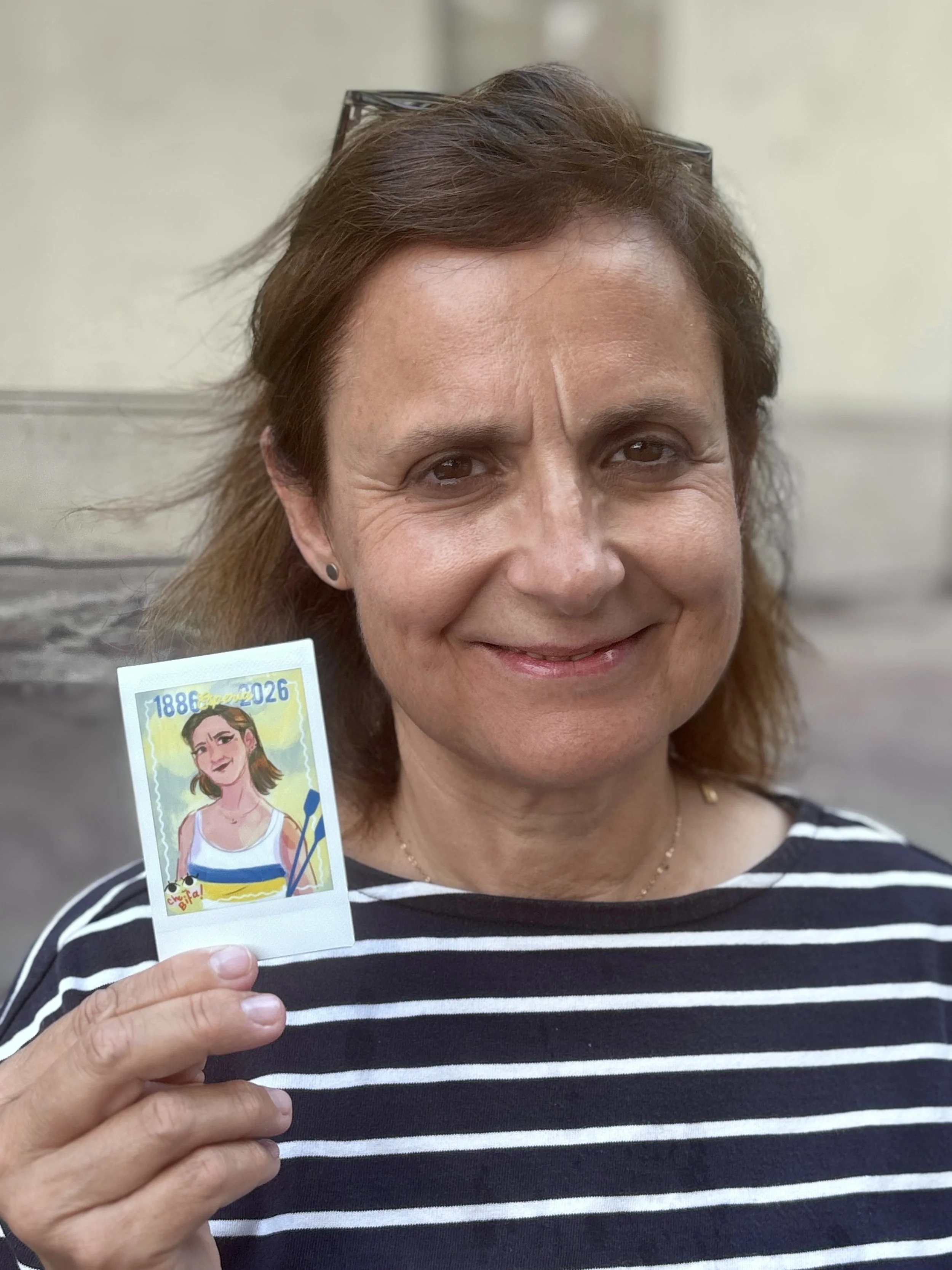 A woman with brown hair and a striped shirt smiling while holding a colorful illustrated stamp featuring a girl in a pattern dress and glasses.