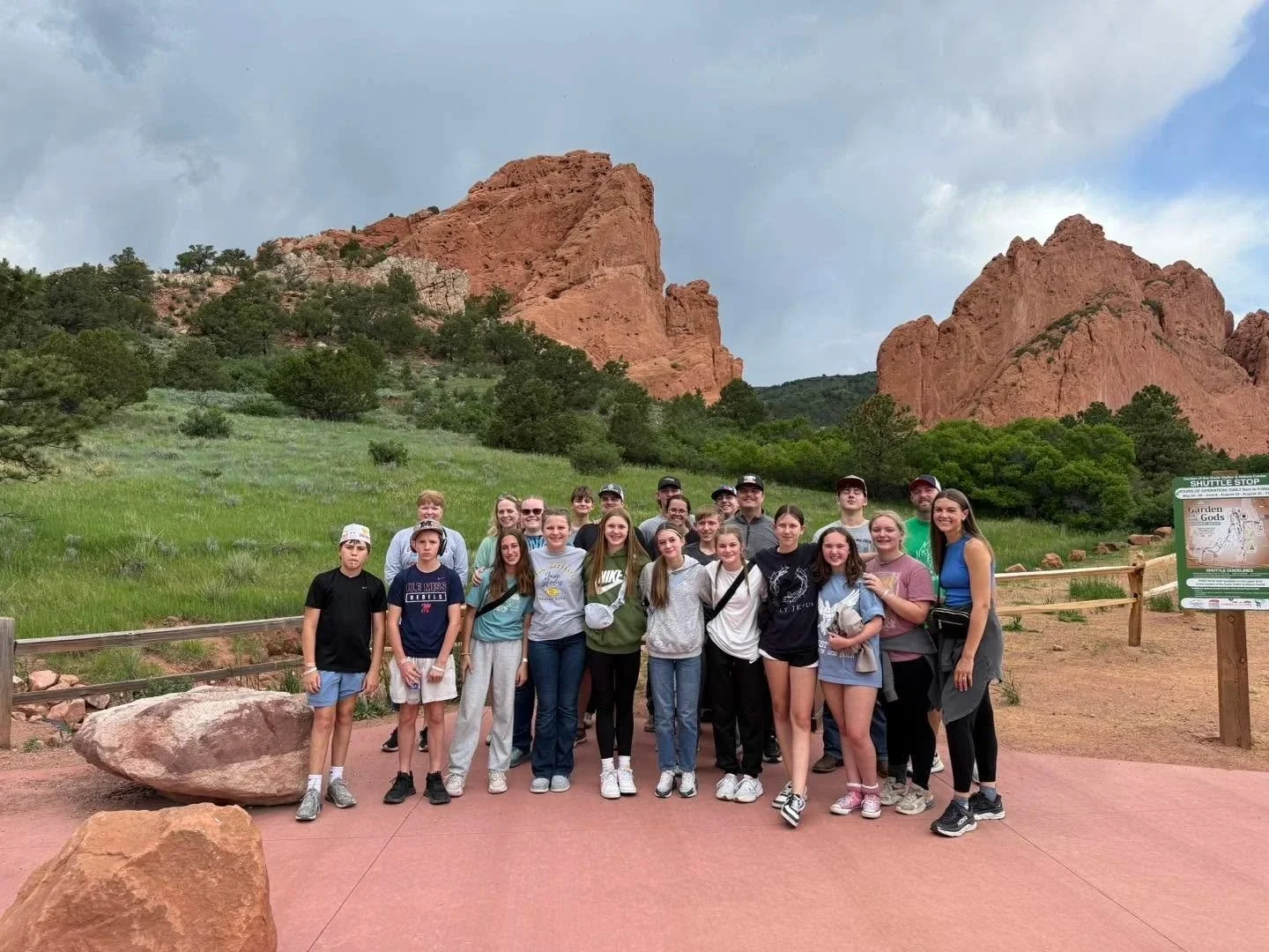 Group of teenagers and adults posing for a photo outdoors, with red rock formations and green trees in the background.