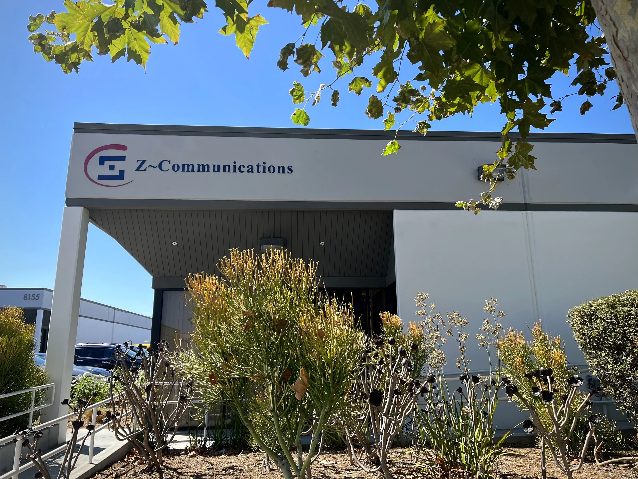 Exterior of Z-Communications building with company sign and surrounding shrubs under a clear blue sky.