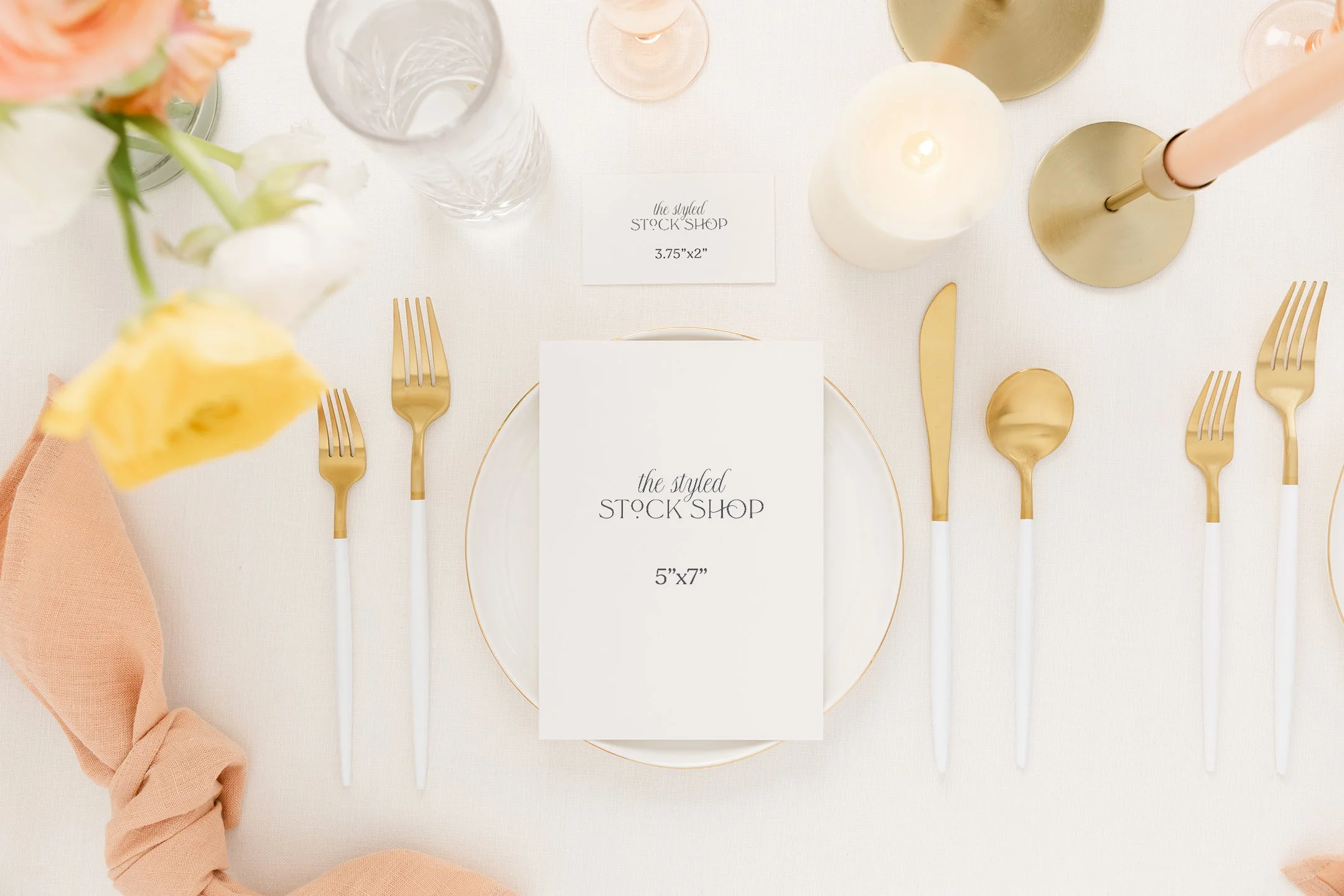 Elegant table setting with gold and white cutlery, a white plate, a menu card, glassware, candles, and flowers on a white tablecloth.