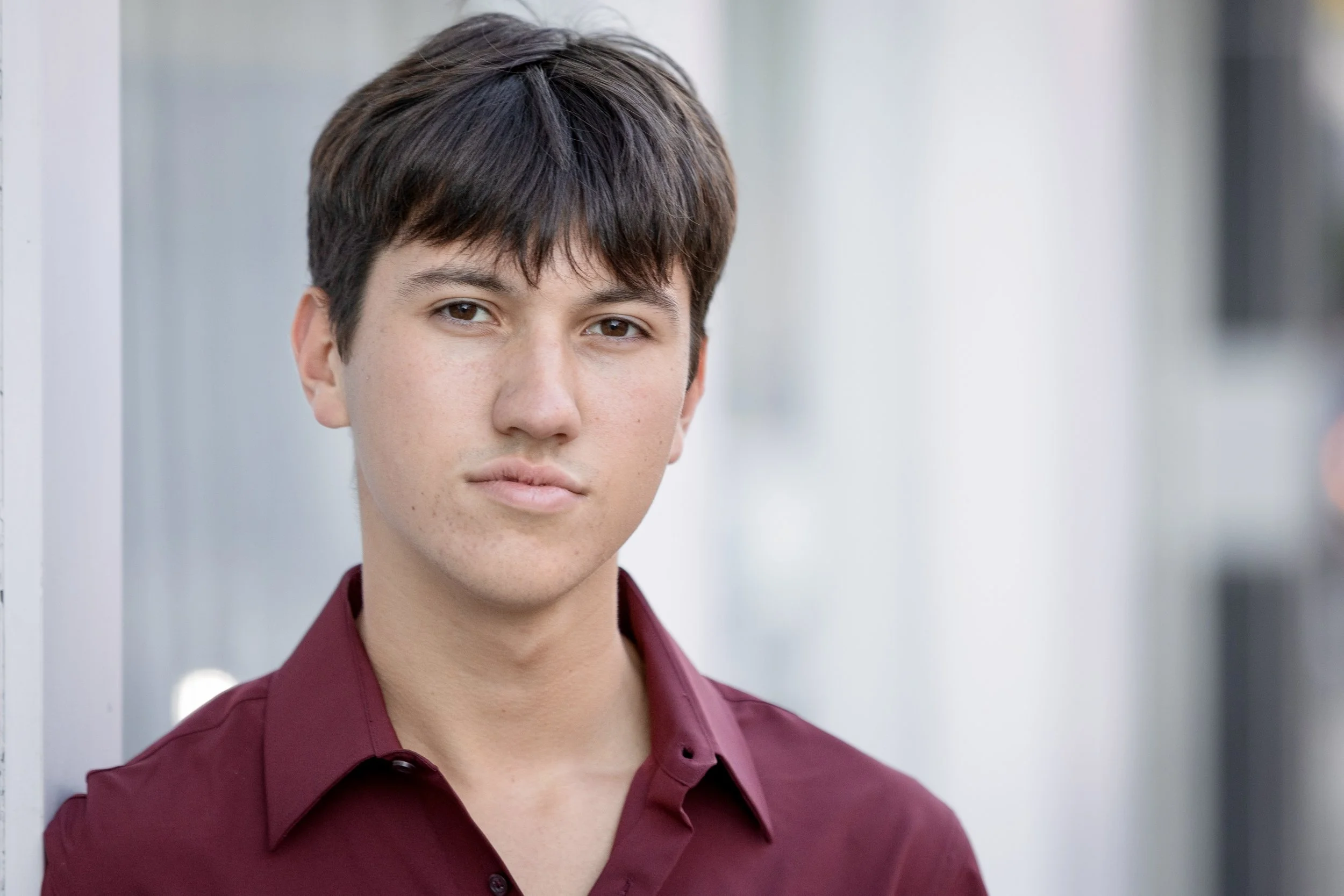 A woman with light skin and shoulder-length red hair, smiling softly, wearing a light gray top, against a blurred gray background.