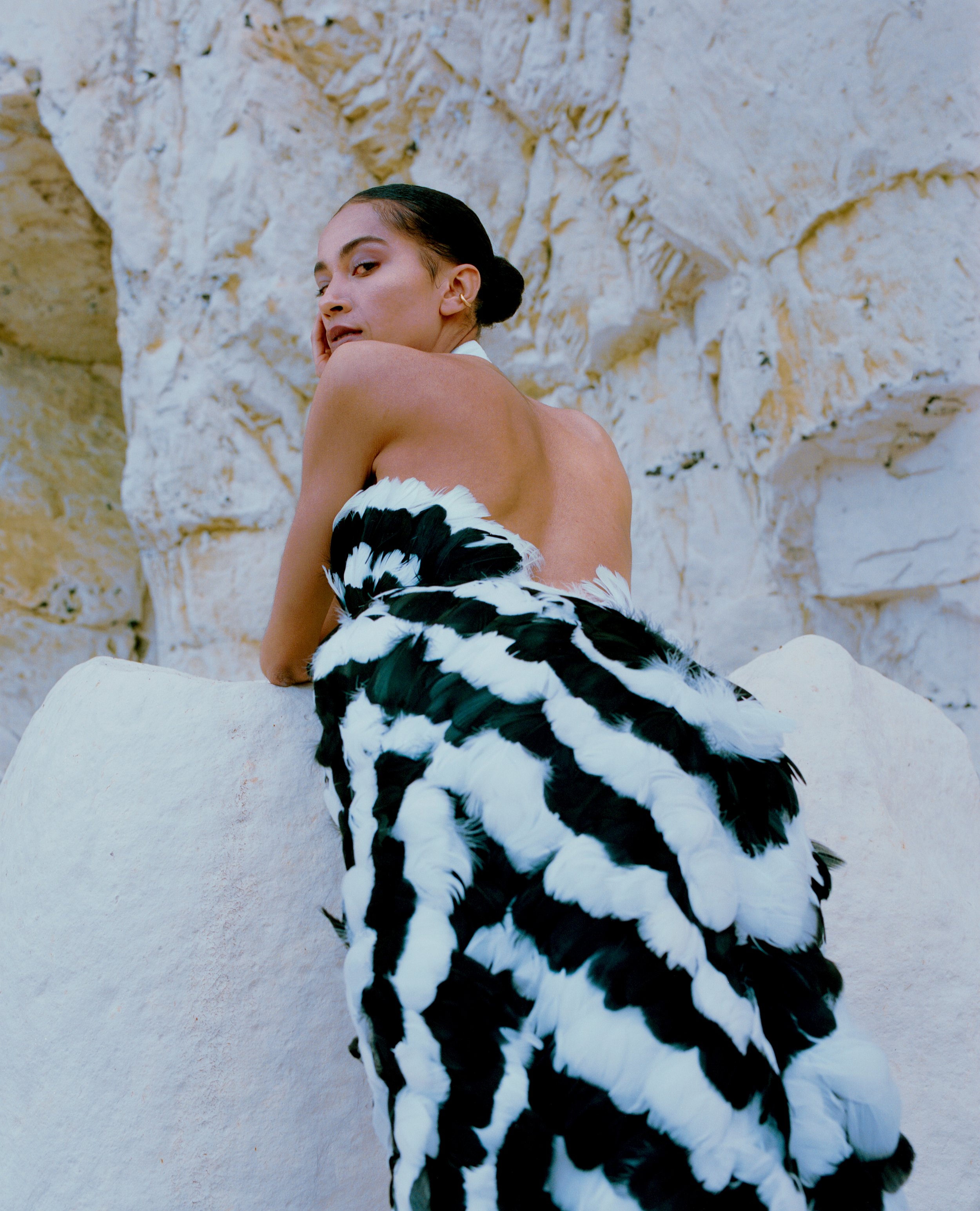 back view of mixed race woman wearing a backless evening gown with black and white feather embroidery